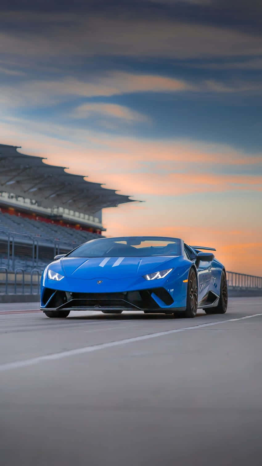 Pixel 3xl Lamborghini 桌布 壁紙 — 一輛充滿活力的藍色藍寶堅尼跑車在日落時分沿著賽道奔馳，背景是觀眾看台。