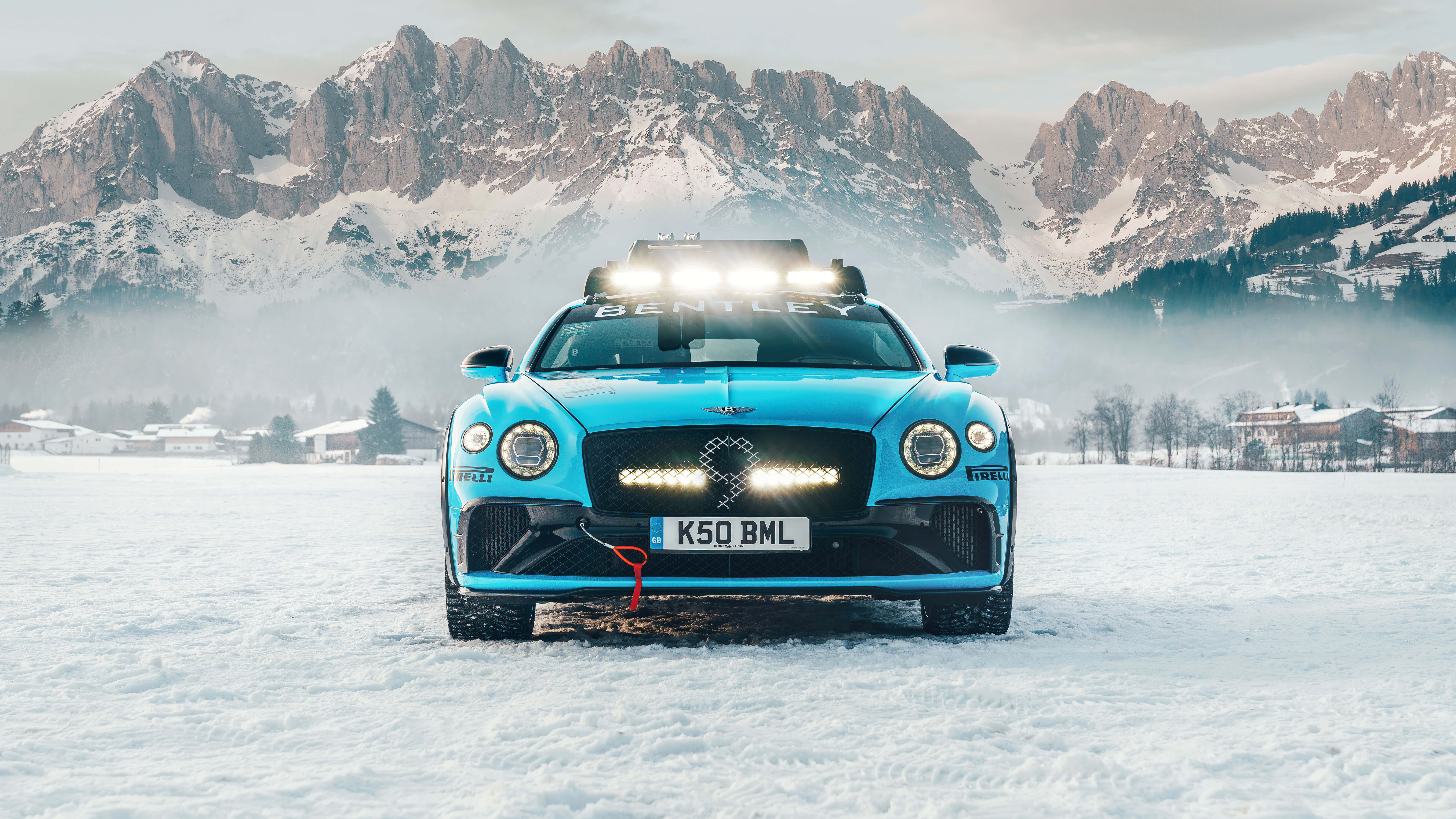 rally 桌布 壁紙 — 一輛充滿活力的藍色賓利 Bentayga 雪地性能車，配備車頂燈，停在雪地上，背景是白雪覆蓋的山脈。