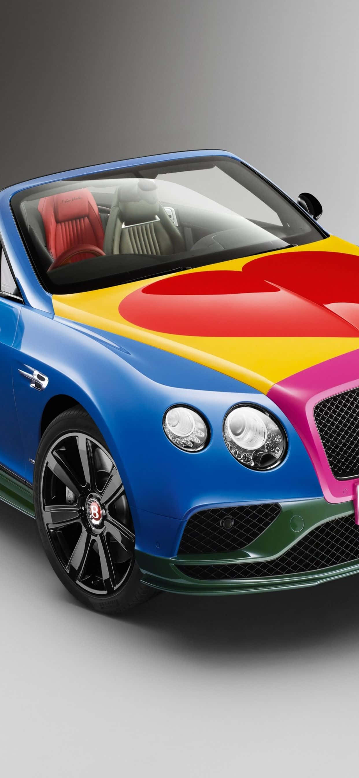 iPhone Xs Max Bentley 桌布 壁紙 — 一輛充滿活力的藍色賓利敞篷車，引擎蓋上有彩虹心形設計，紅色皮革內飾。
