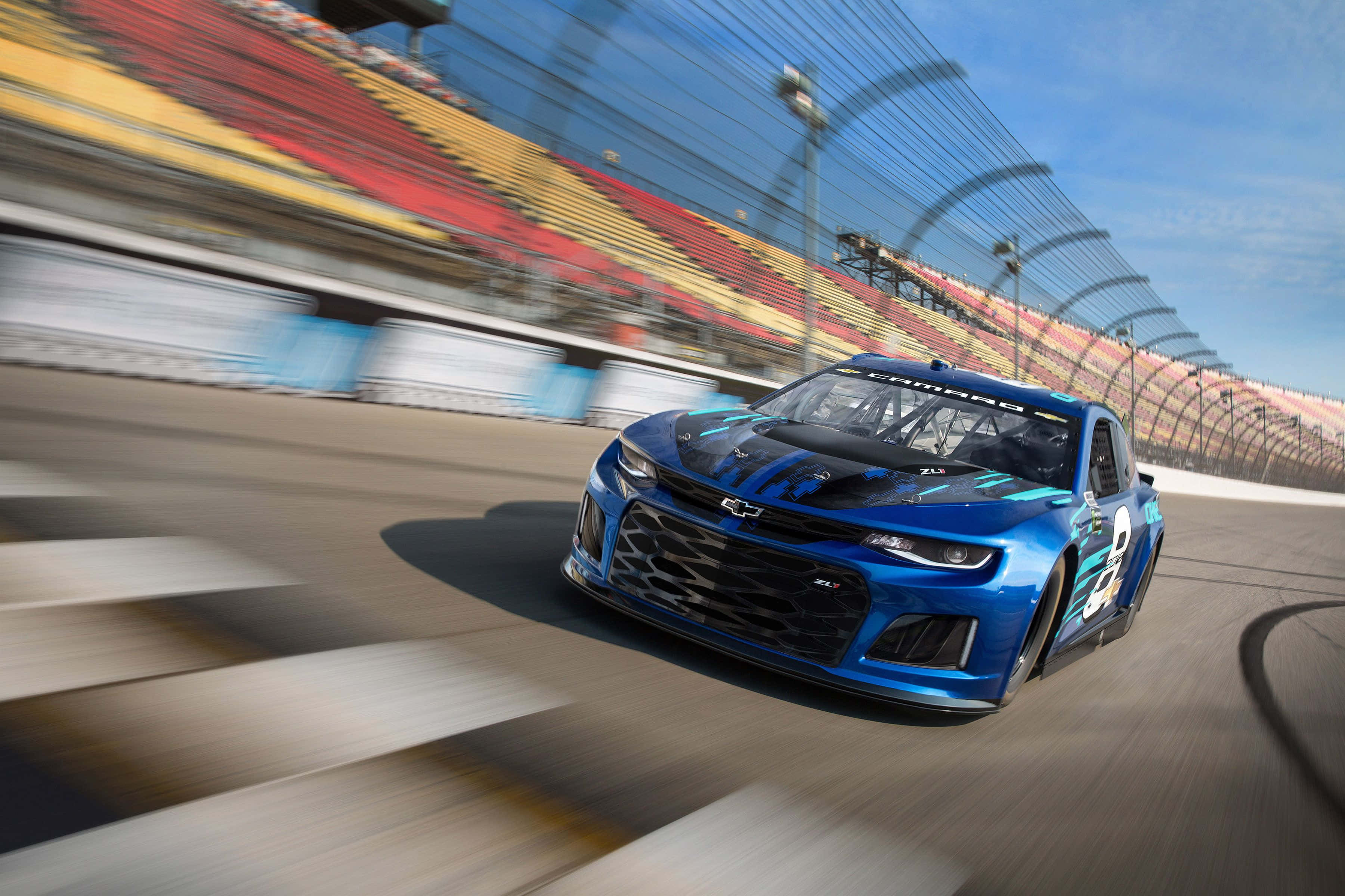nascar 桌布 壁紙 — 一輛充滿活力的藍色賽車在晴朗的藍天下，在帶有模糊看台的賽道上飛馳。