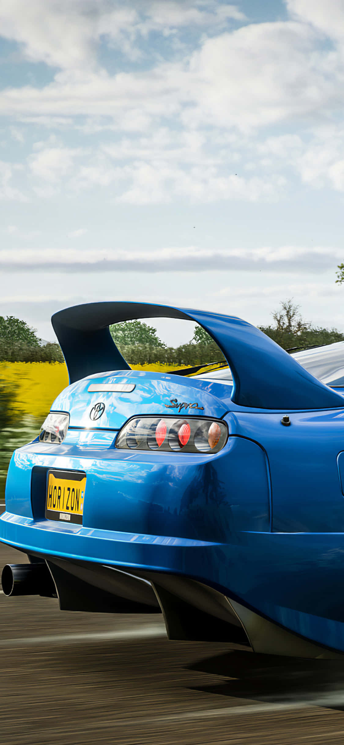 Pixel 3 Forza Horizon 4 桌布 壁紙 — 一輛充滿活力的藍色跑車，帶有大型後擾流板，在部分多雲的天空下，沿著一條穿過金色田野的道路疾馳。