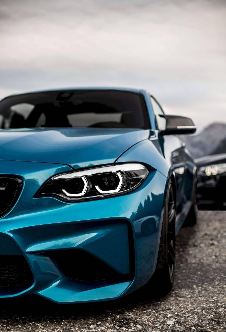 Bmw Cars 桌布 壁紙 — 一輛充滿活力的藍色跑車，配備時尚車頭燈，停泊在碎石路上，背景是陰天。