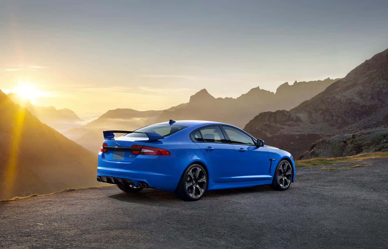 Jaguar Xfr 桌布 壁紙 — 一輛充滿活力的藍色跑車停在山路上，太陽在崎嶇的山峰上升起。