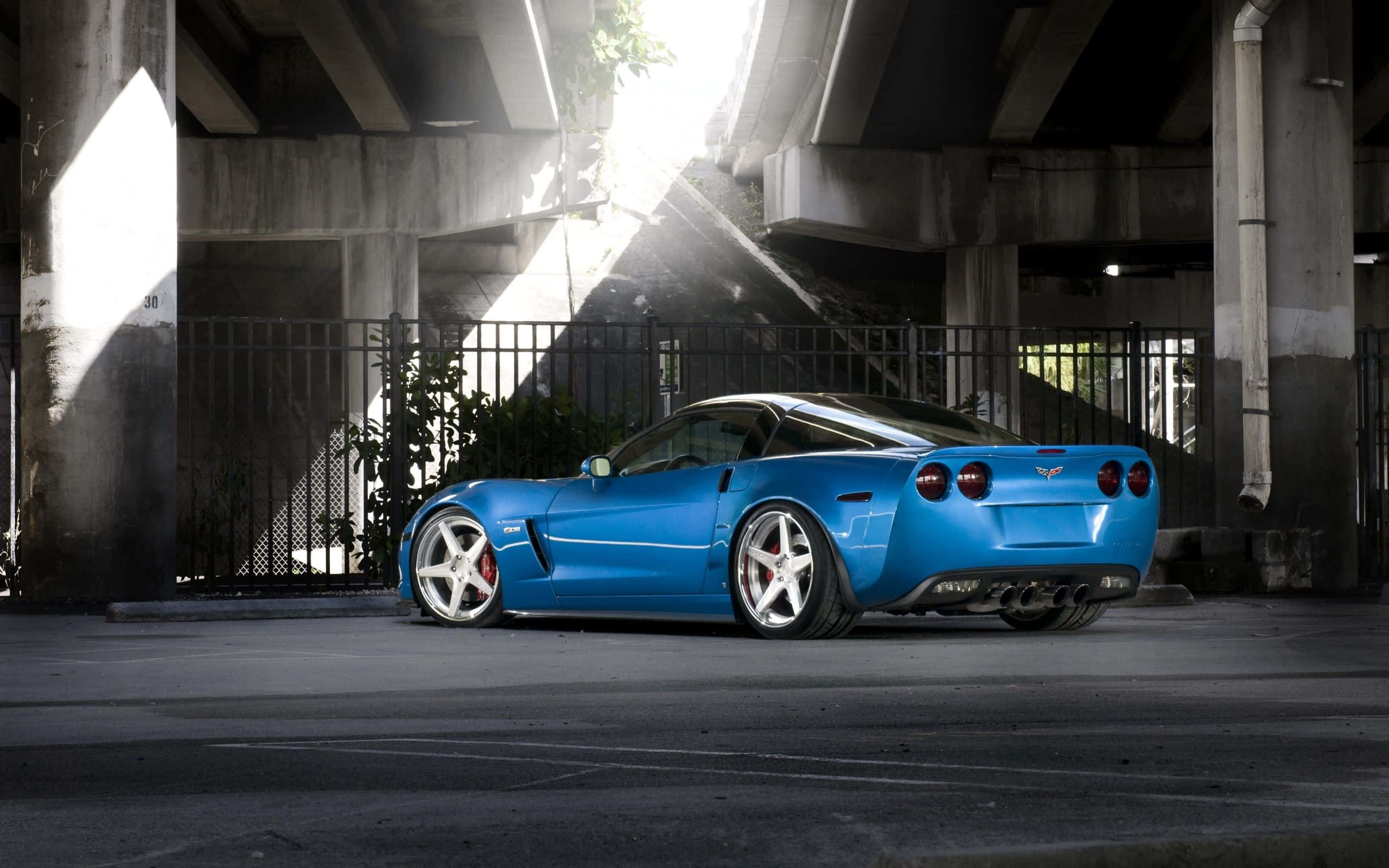 Chevrolet Corvette Z06 桌布 壁紙 — 一輛充滿活力的藍色跑車停放在城市高架橋下，戲劇性的陽光穿過混凝土樑柱。