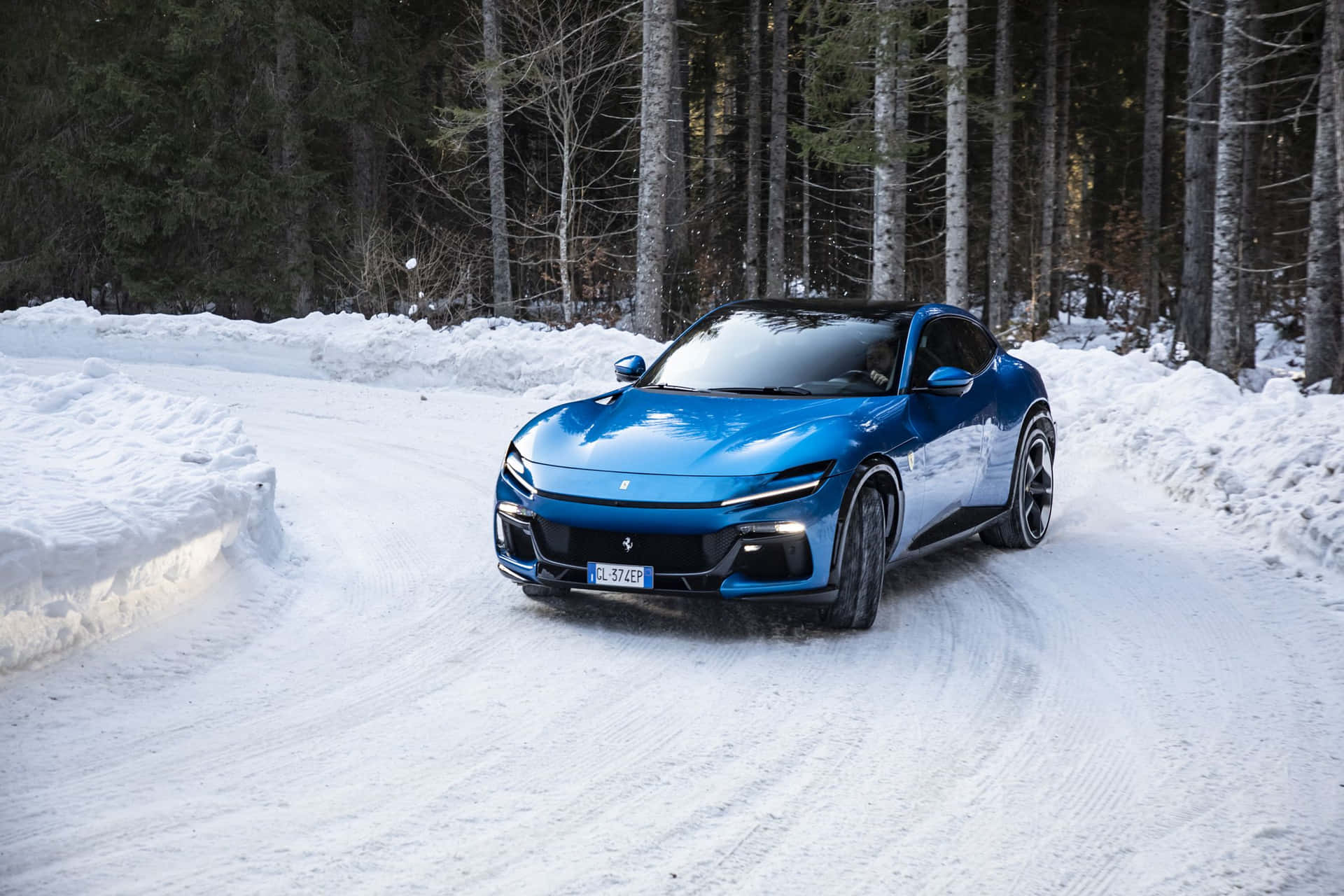  壁紙 — 一輛充滿活力的藍色跑車在白雪覆蓋的森林道路上行駛，兩旁是高聳的松樹。