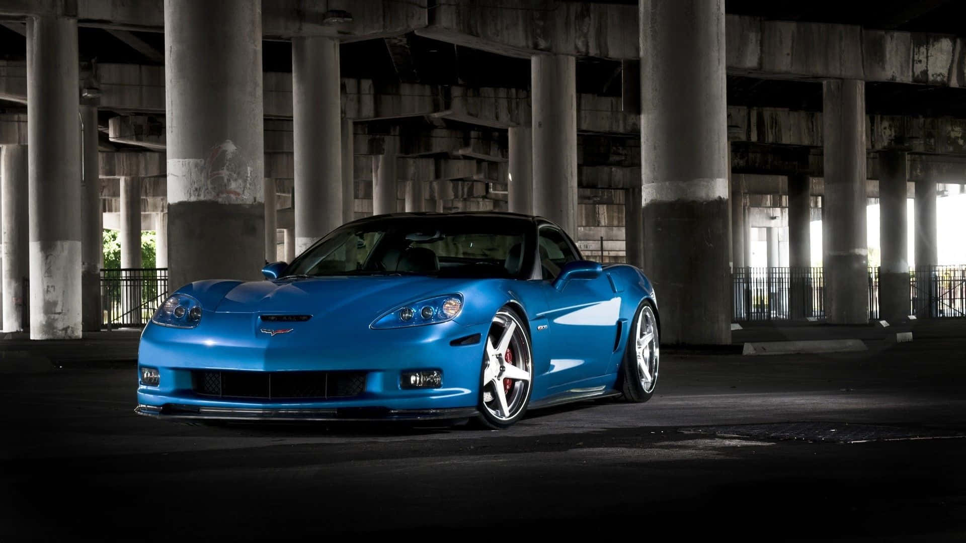 Chevrolet Corvette Z06 桌布 壁紙 — 一輛充滿活力的藍色跑車在破舊的混凝土天橋下，在戲劇性的燈光下閃閃發光。
