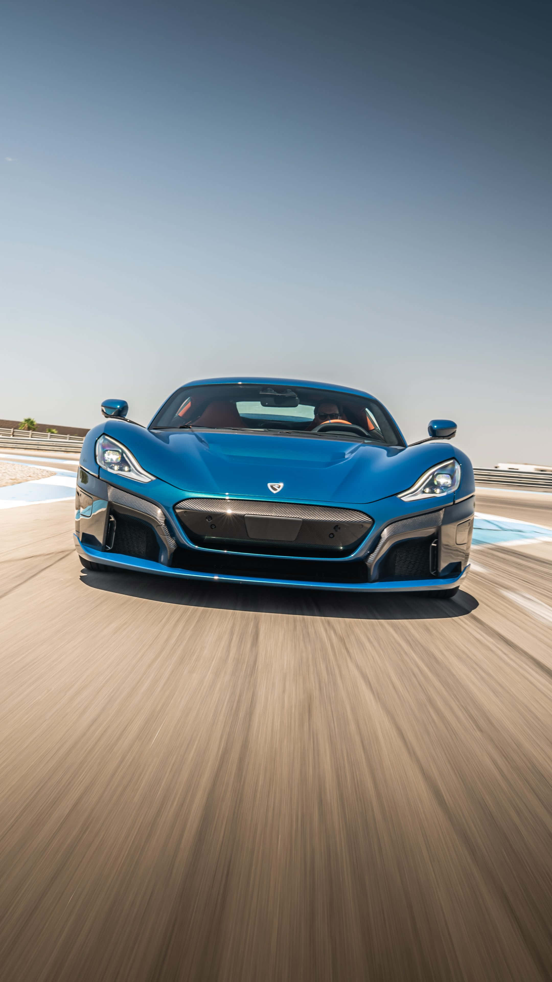 Rimac 桌布 壁紙 — 一輛充滿活力的藍色跑車在陽光照耀的賽道上疾馳，動態模糊強調了速度。