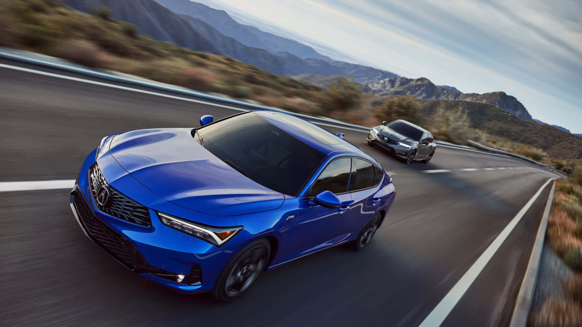 Acura Integra 桌布 壁紙 — 一輛充滿活力的藍色轎車在晴朗的天空下沿著蜿蜒的山路疾馳，後面跟著一輛銀色汽車。
