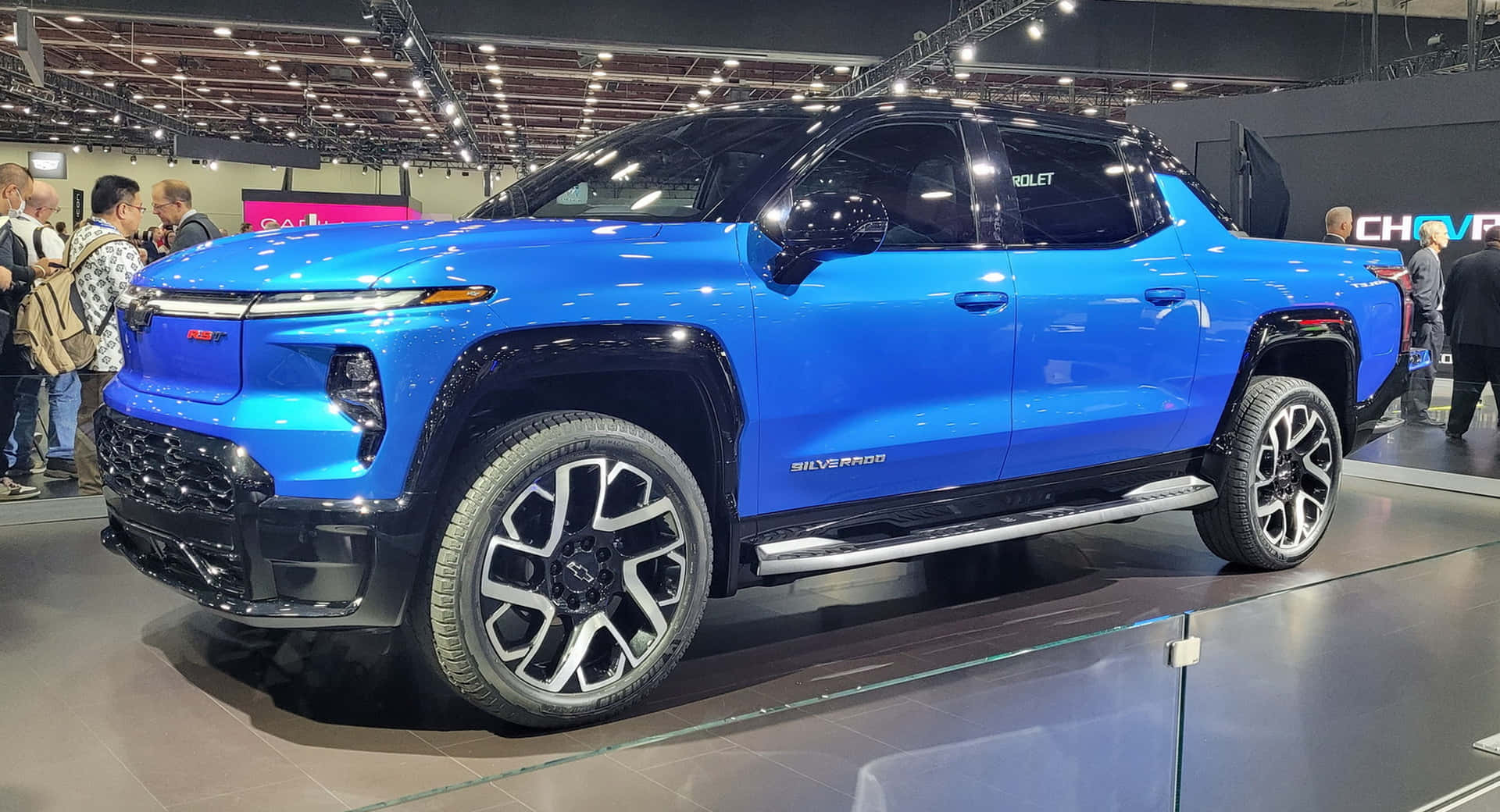 Chevrolet 桌布 壁紙 — 一輛充滿活力的藍色雪佛蘭Silverado皮卡在繁忙的車展上，在明亮的展覽燈光下閃閃發光。