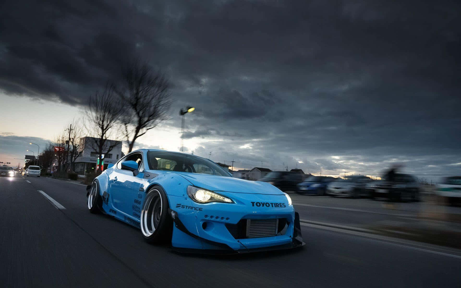 一輛藍色飄移車在暮色中沿著潮濕的城市街道疾馳。 — Toyota Supra Mk4 壁紙