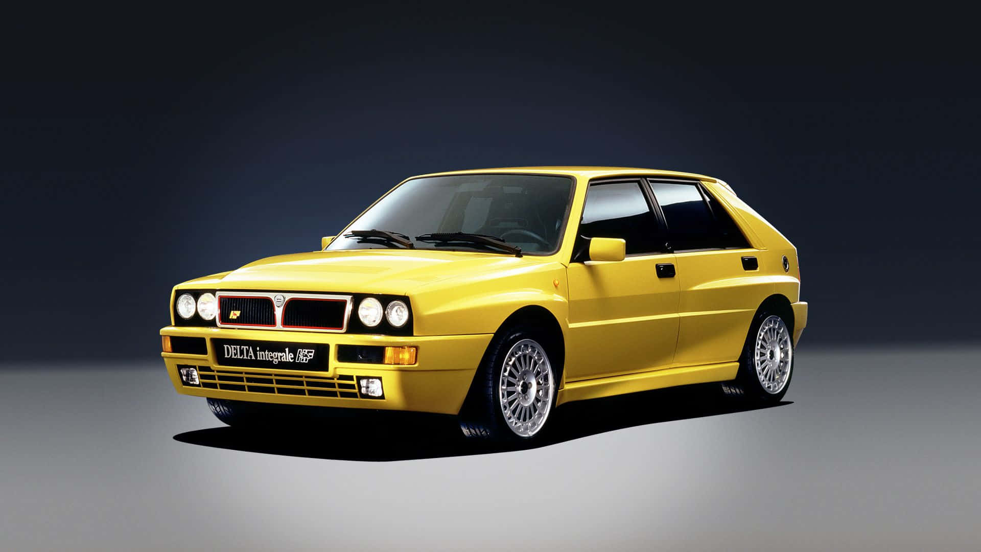 Lancia 桌布 壁紙 — 一輛充滿活力的黃色 Lancia Delta Integrale 16V 跑車在黑暗的攝影棚背景下，搭配戲劇性的燈光。