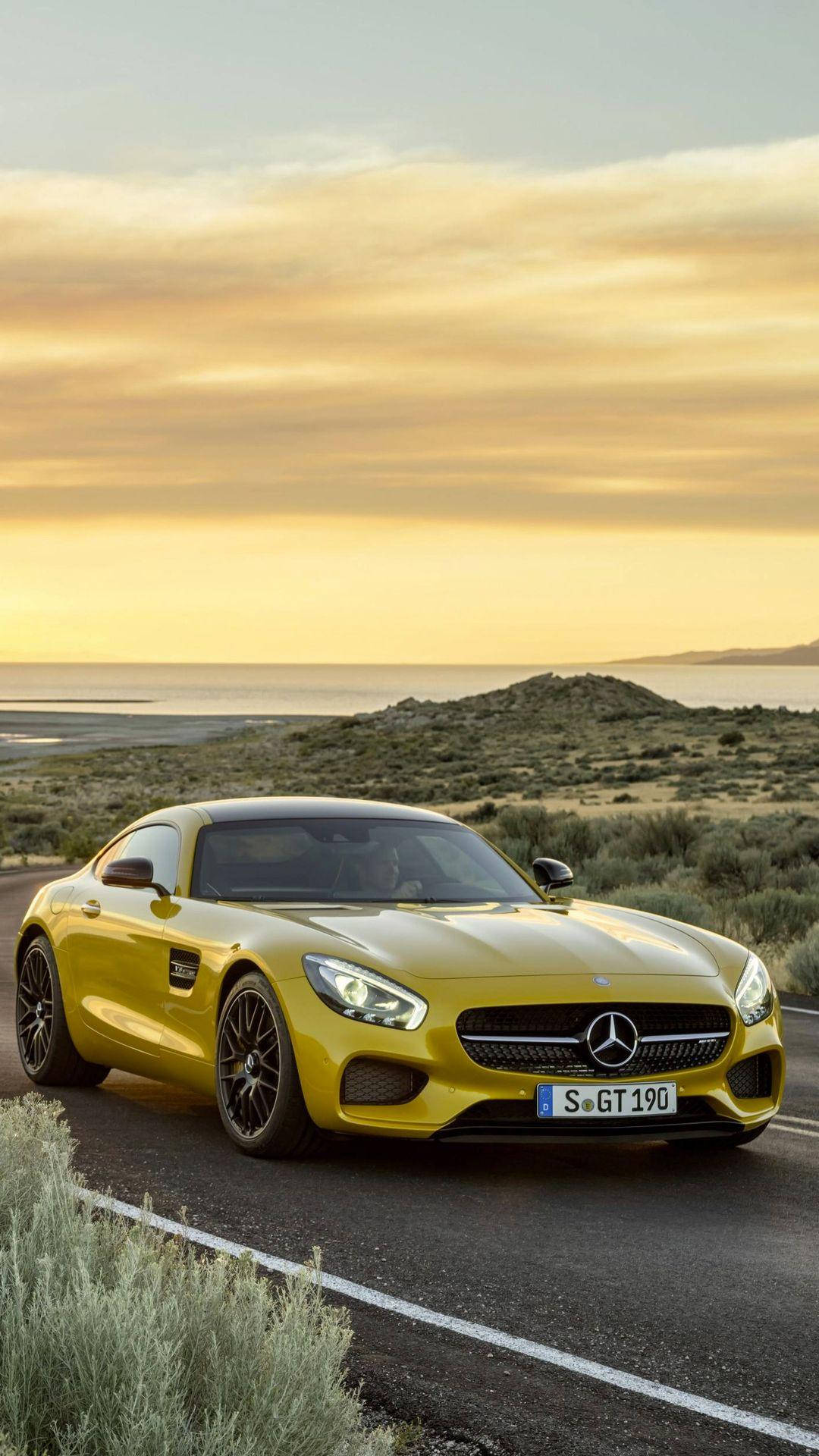 X 桌布 壁紙 — 一輛充滿活力的黃色 Mercedes-AMG GT 跑車停泊在海岸公路上，正值黃金時刻，背景是寧靜的海洋。