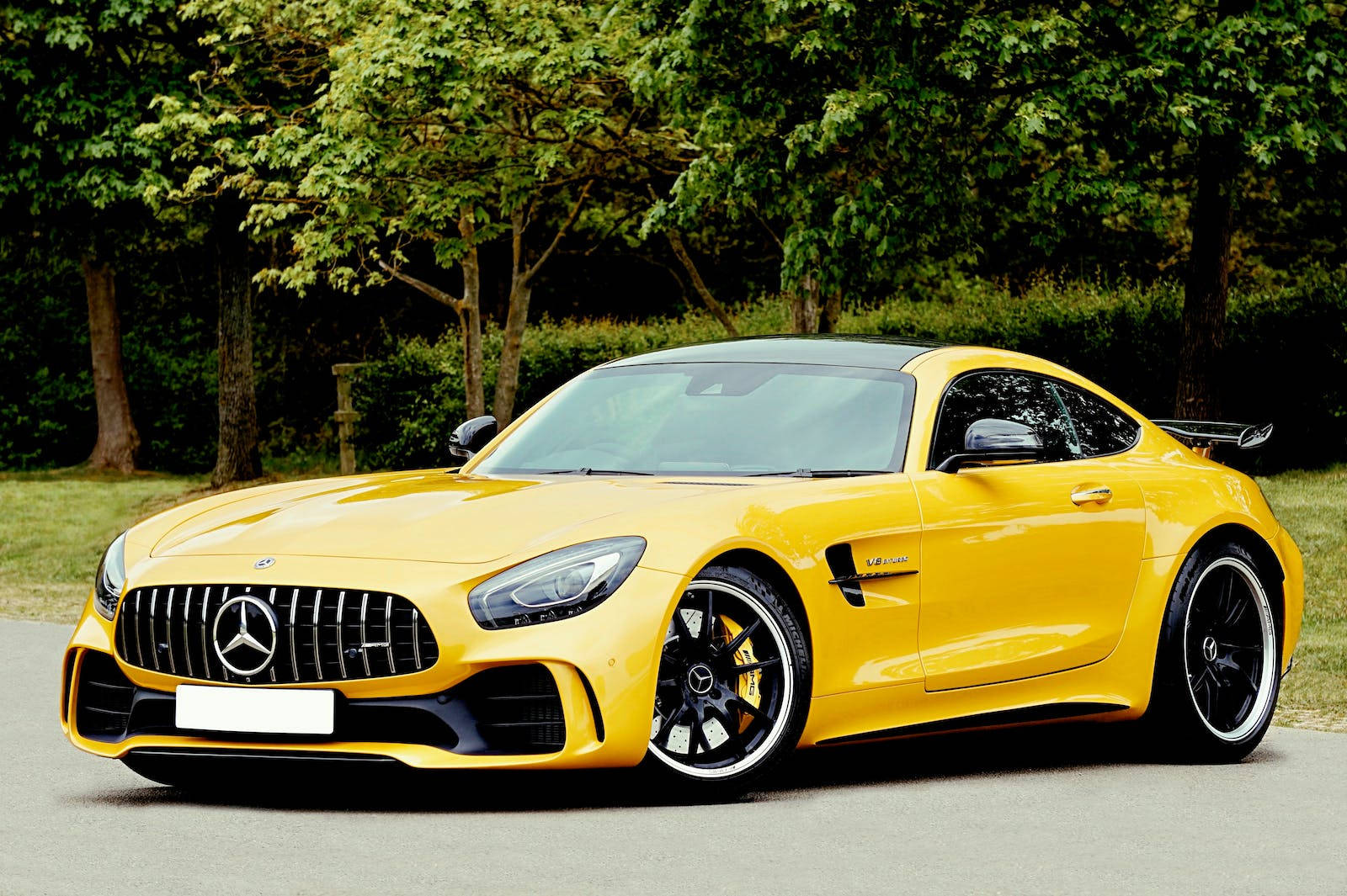 跑車 桌布 壁紙 — 一輛充滿活力的黃色 Mercedes-AMG GT R 跑車停放在鋪砌的道路上，背景是茂密的綠樹。