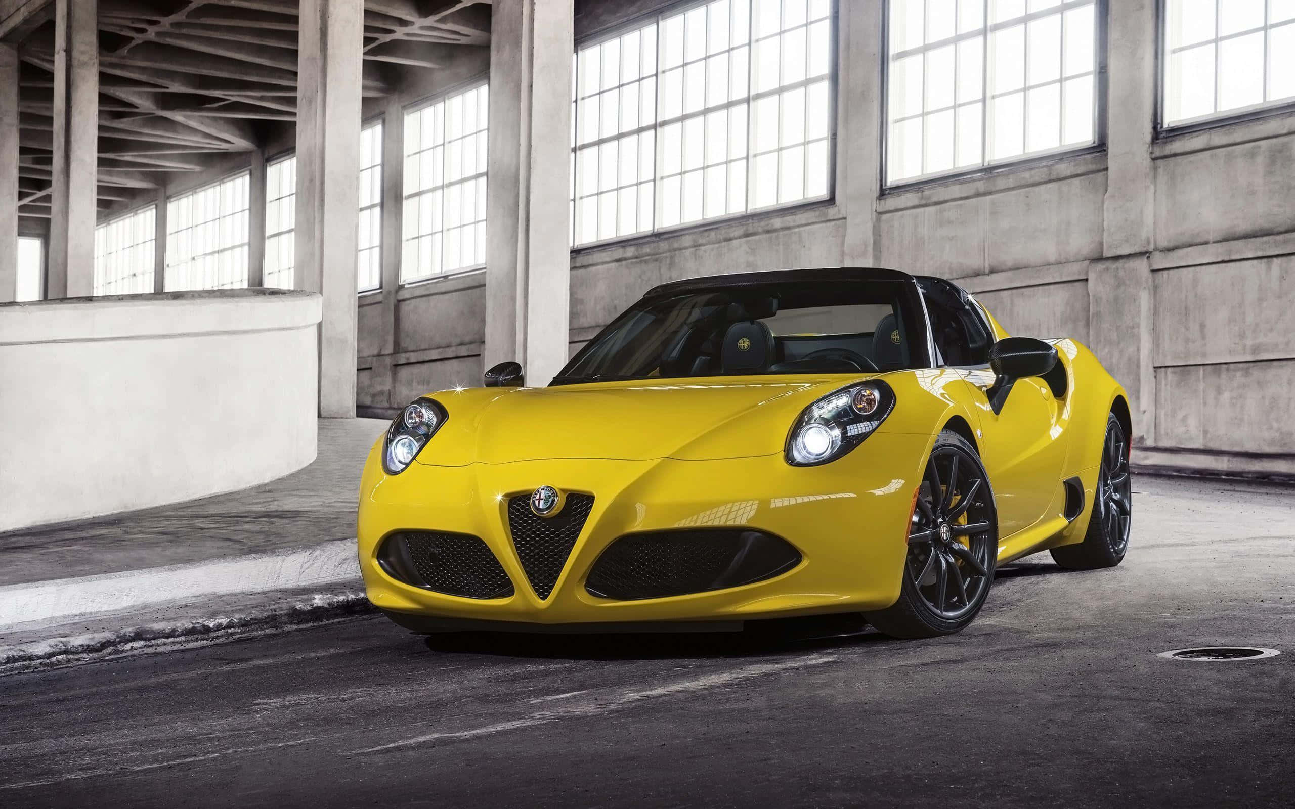 Alfa Romeo 4c 桌布 壁紙 — 一輛充滿活力的黃色Alfa Romeo 4C跑車在寬敞的混凝土倉庫內，透過大窗戶的自然光下閃閃發光。