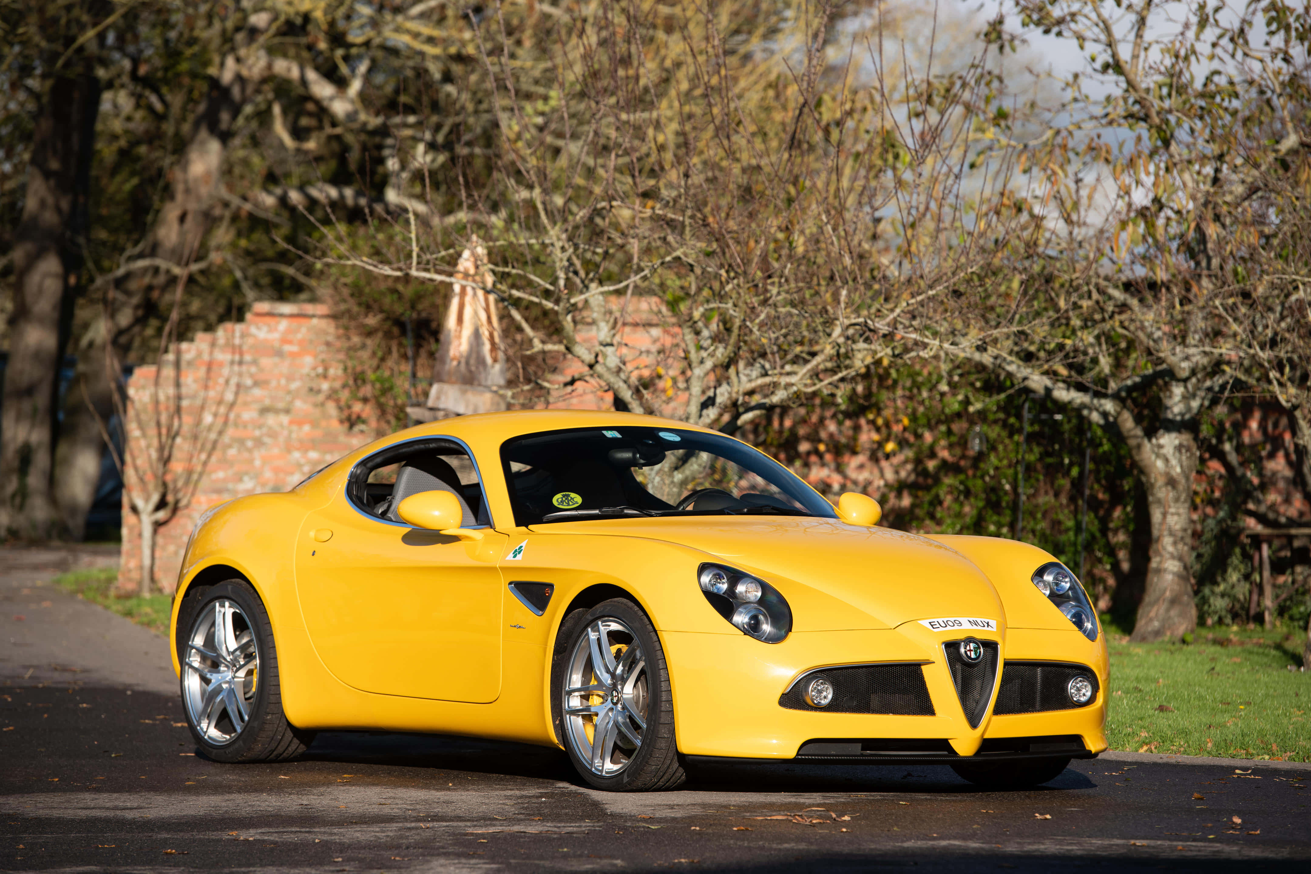Alfa Romeo 8c Competizione 桌布 壁紙 — 一輛充滿活力的黃色Alfa Romeo跑車停泊在林蔭大道上，背景有秋葉和磚牆。