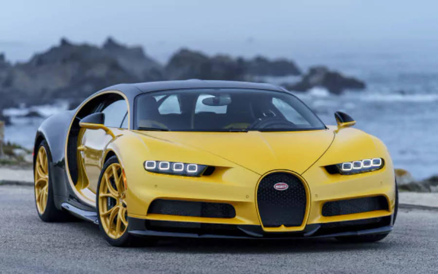 4K 桌布 壁紙 — 一輛充滿活力的黃色Bugatti Chiron配金色輪圈，停泊在海岸公路上，旁邊是拍岸的浪濤和岩石峭壁。
