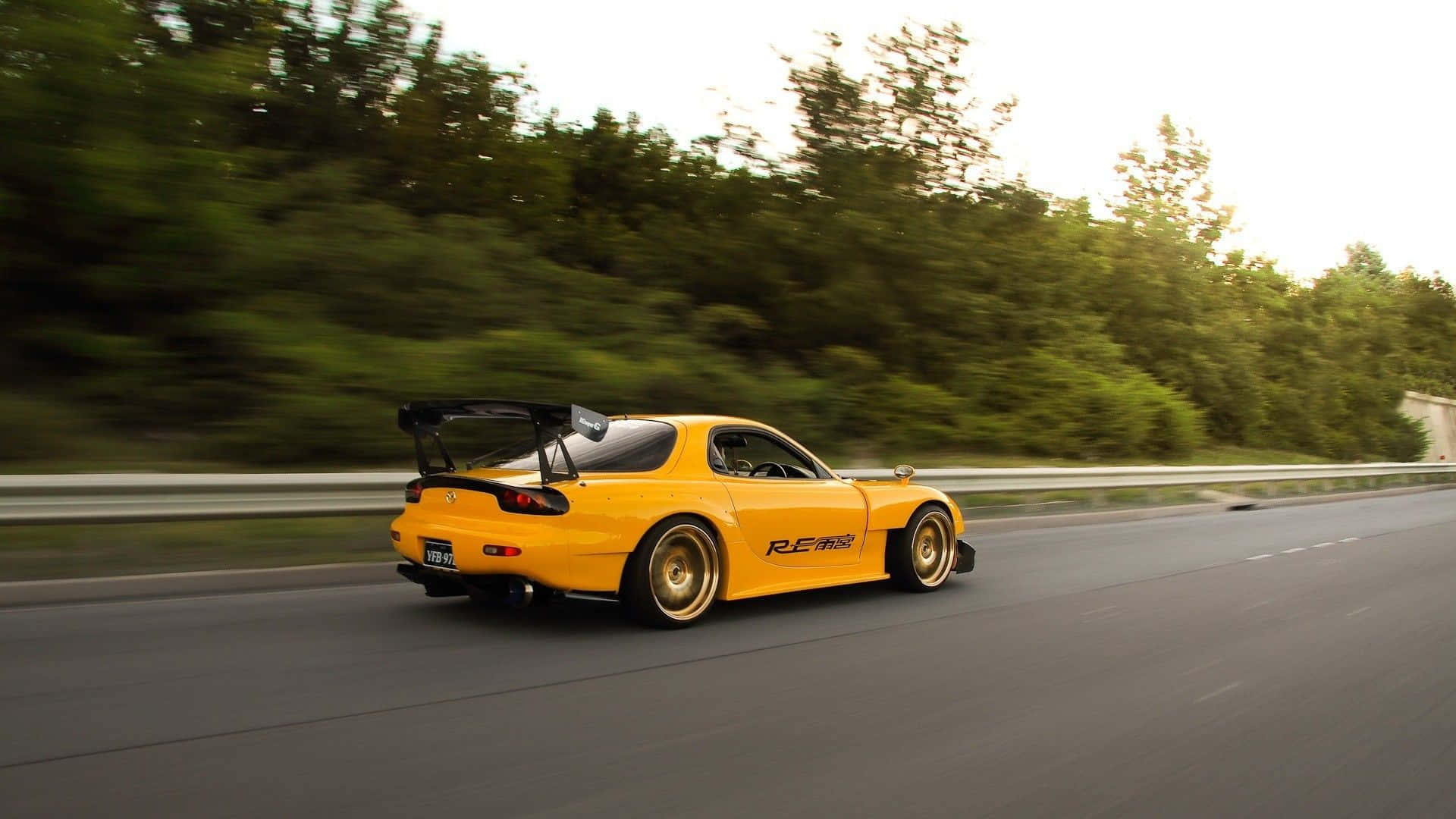 Mazda 桌布 壁紙 — 一輛充滿活力的黃色Mazda RX-7跑車在綠樹成蔭的高速公路上疾馳，動態模糊傳達出高速感。
