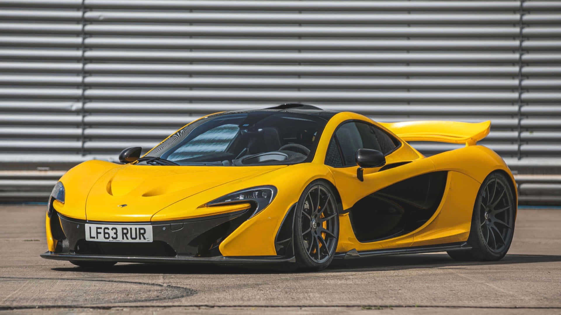 麥拉倫 桌布 壁紙 — 一輛充滿活力的黃色McLaren P1超級跑車，帶有黑色飾邊，停在賽道上，旁邊是波紋金屬護欄。