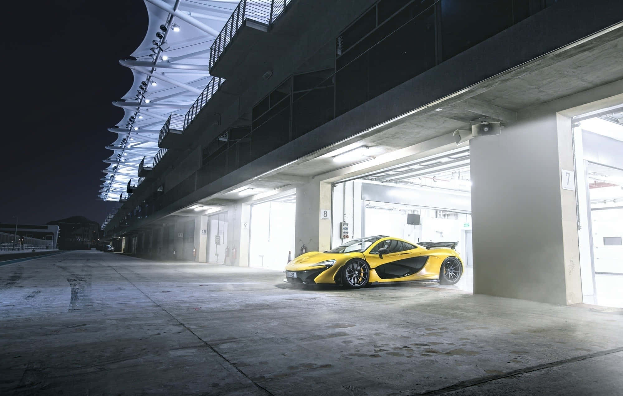 Building 桌布 壁紙 — 一輛充滿活力的黃色McLaren跑車在夜間賽車場的明亮車庫燈光下閃閃發光。
