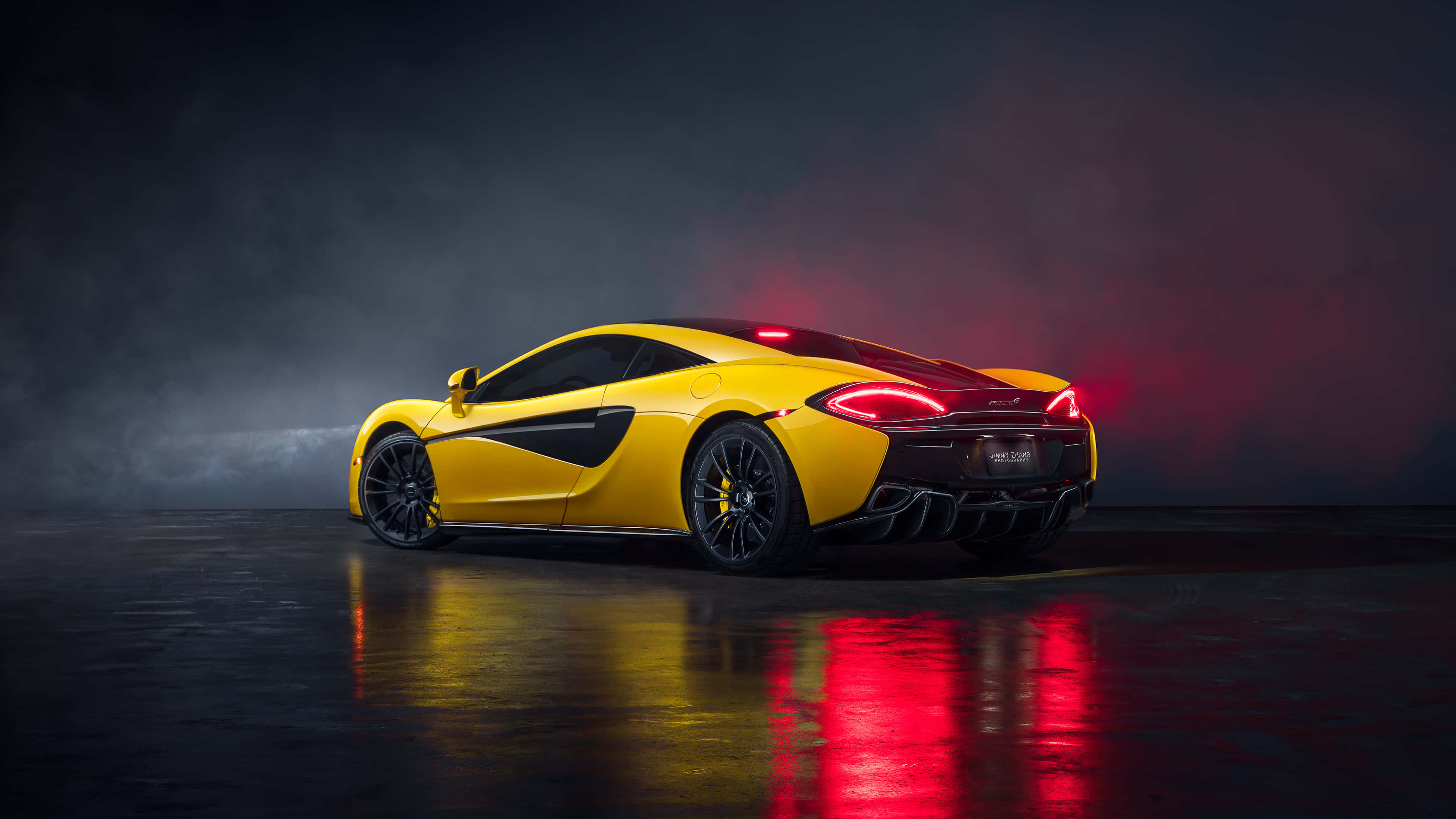 Cool Mclaren 桌布 壁紙 — 一輛充滿活力的黃色McLaren跑車，在帶有反射地板的煙霧瀰漫的黑暗工作室背景下，紅色尾燈閃閃發光。