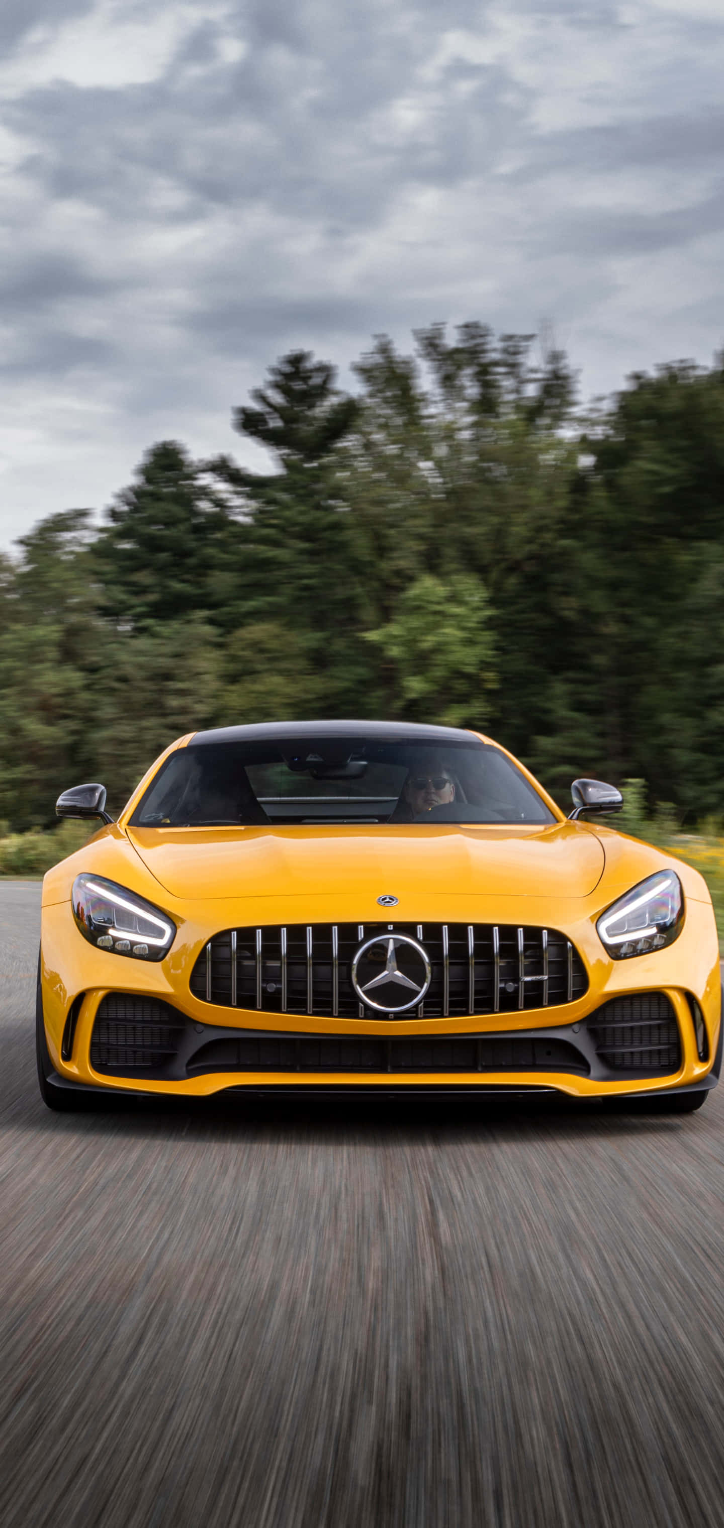 Mercedes 桌布 壁紙 — 一輛充滿活力的黃色Mercedes-AMG GT在陰天下行駛在森林道路，帶有動態模糊效果。