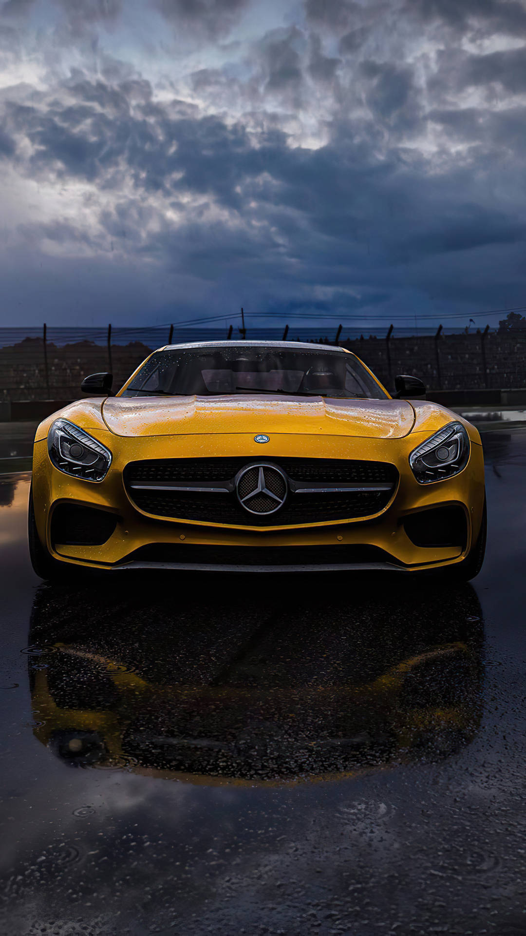 賓士 iPhone 桌布 壁紙 — 一輛充滿活力的黃色Mercedes-AMG GT跑車在潮濕的賽道上閃閃發光，背景是戲劇性的暴風雨天空，反射出鮮明的倒影。