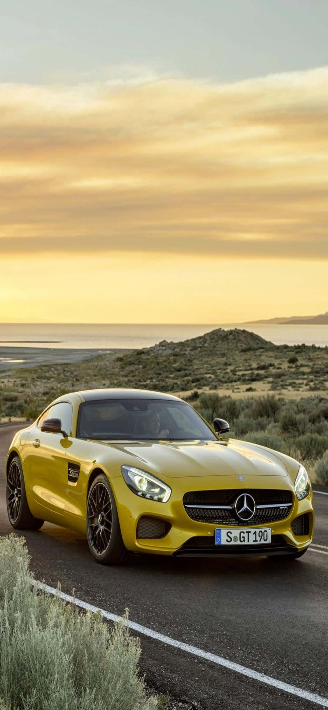 Mercedes 桌布 壁紙 — 一輛充滿活力的黃色Mercedes-AMG GT跑車在黃金時段沿著海岸公路行駛，背景是寧靜的海洋。
