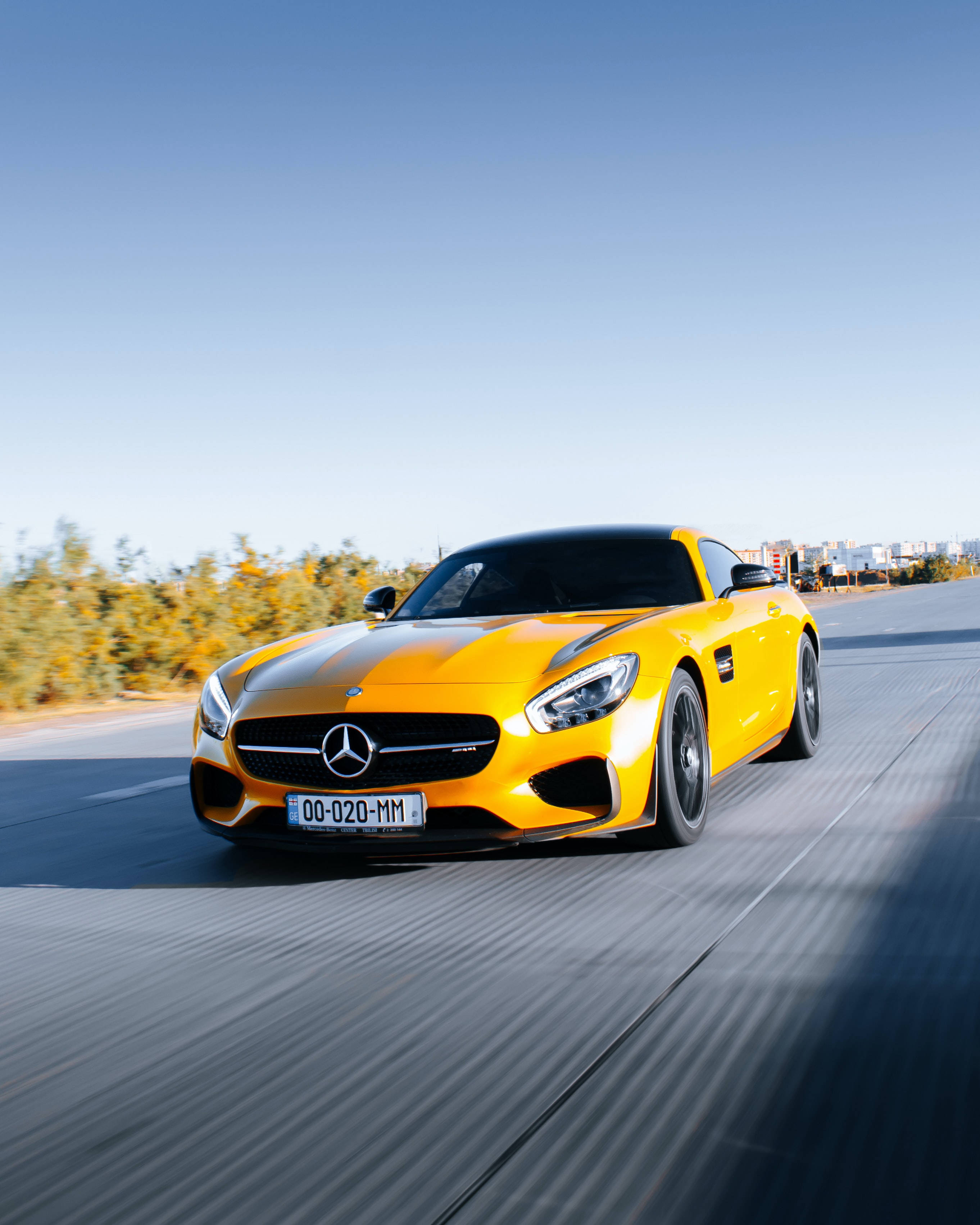 Gtr 桌布 壁紙 — 一輛充滿活力的黃色Mercedes-AMG GT S在陽光照耀的道路上疾馳，背景有模糊的動感和秋天的樹木。