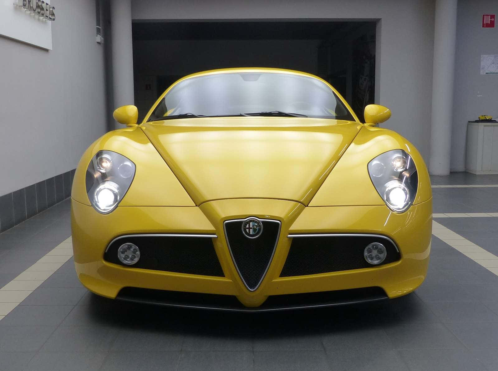 Alfa Romeo 8c Competizione 桌布 壁紙 — 一輛充滿活力的黃色愛快羅密歐跑車在明亮的燈光下於時尚的現代車庫中閃閃發光。
