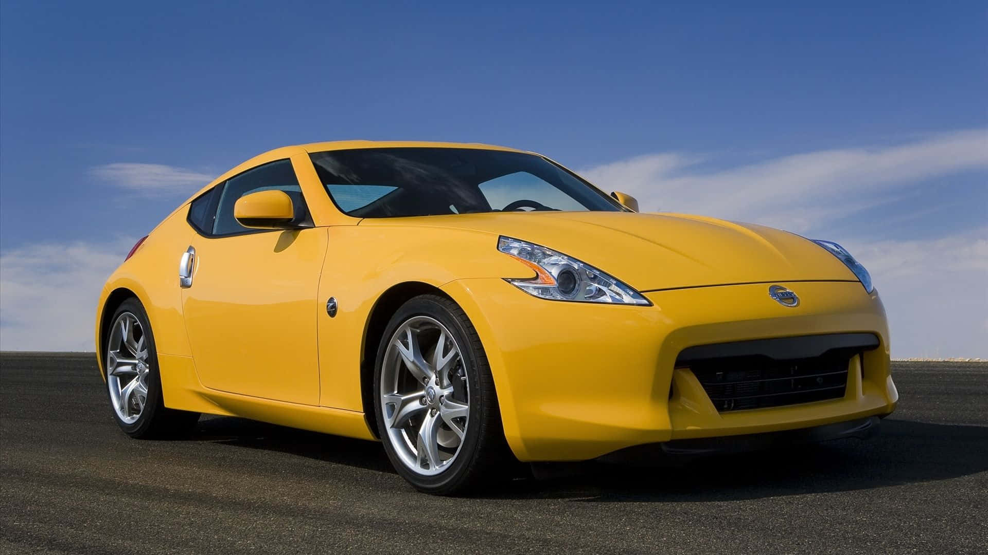 Yellow Car 桌布 壁紙 — 一輛充滿活力的黃色日產370Z跑車在晴朗藍天下，在開闊的瀝青路上閃閃發光。