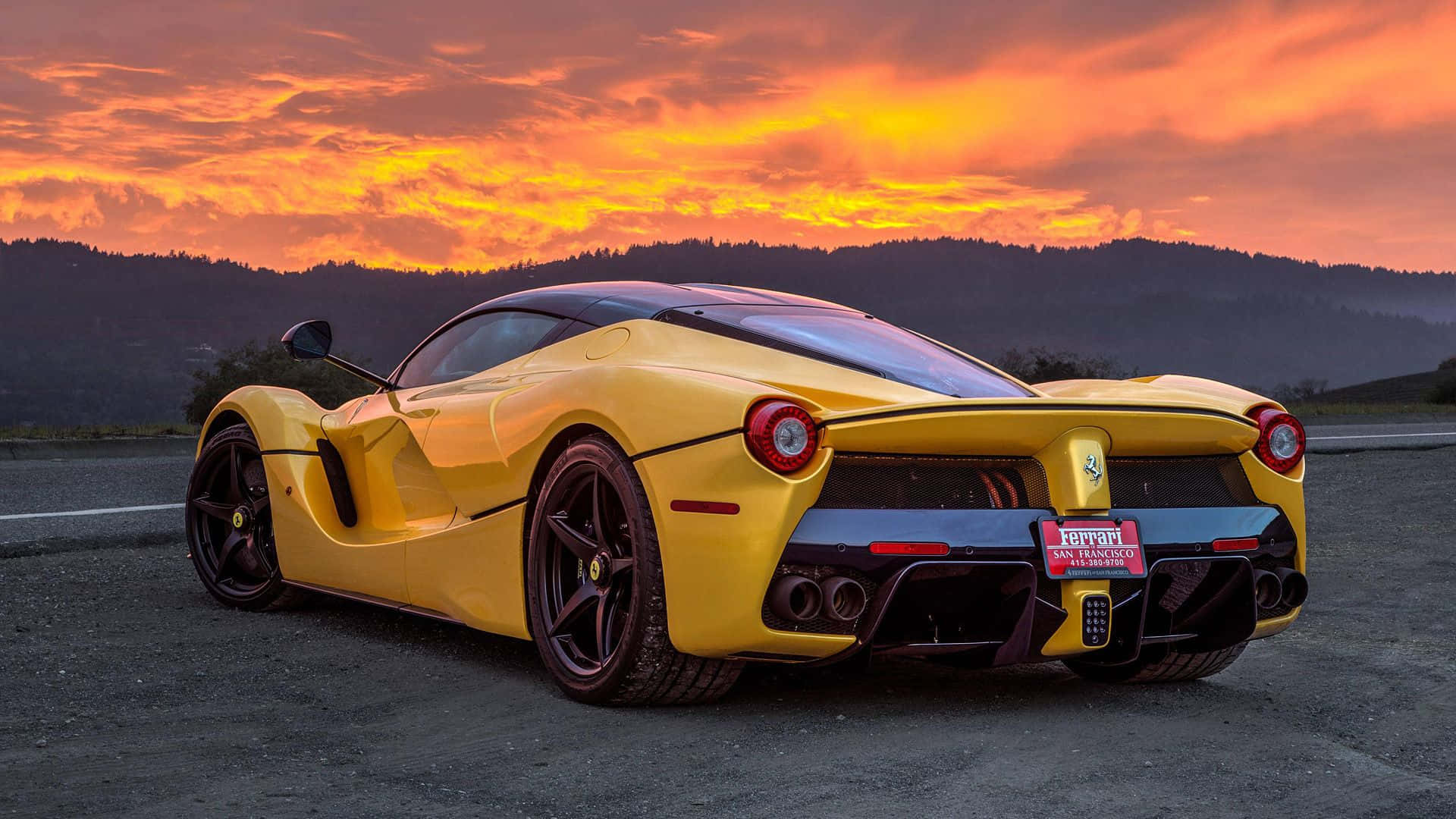 Ferrari Laferrari 桌布 壁紙 — 一輛充滿活力的黃色法拉利LaFerrari停在瀝青路上，背景是火紅的橙色和粉紅色日落天空，遠處有山丘。