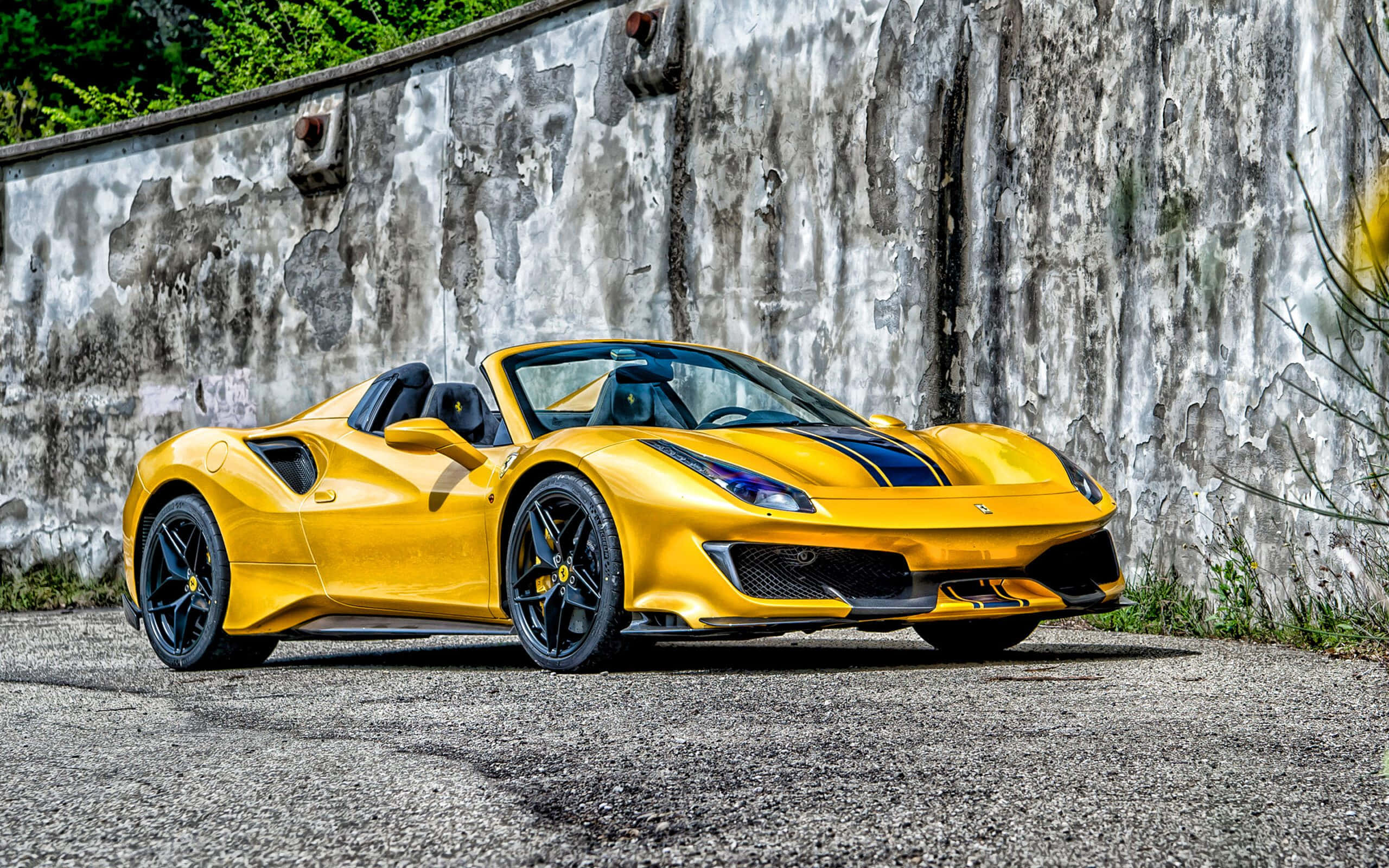 Ferrari 488 Spider 桌布 壁紙 — 一輛充滿活力的黃色法拉利跑車，帶有黑色裝飾，停在碎石地上，旁邊是一面風化的混凝土牆。
