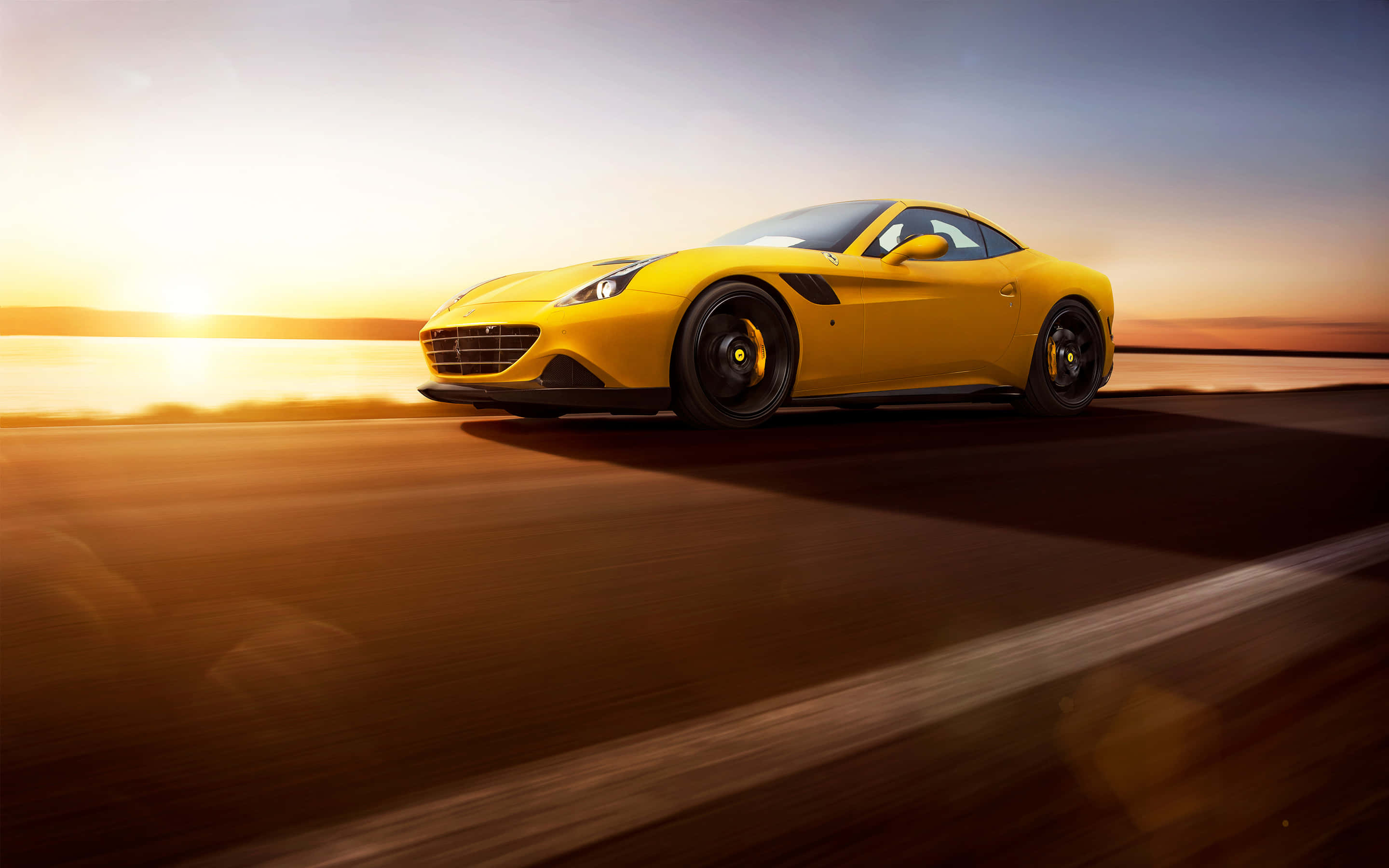 Ferrari California T 桌布 壁紙 — 一輛充滿活力的黃色法拉利跑車在日落時分沿著海岸公路疾馳，伴隨著金色光芒和動態模糊效果。