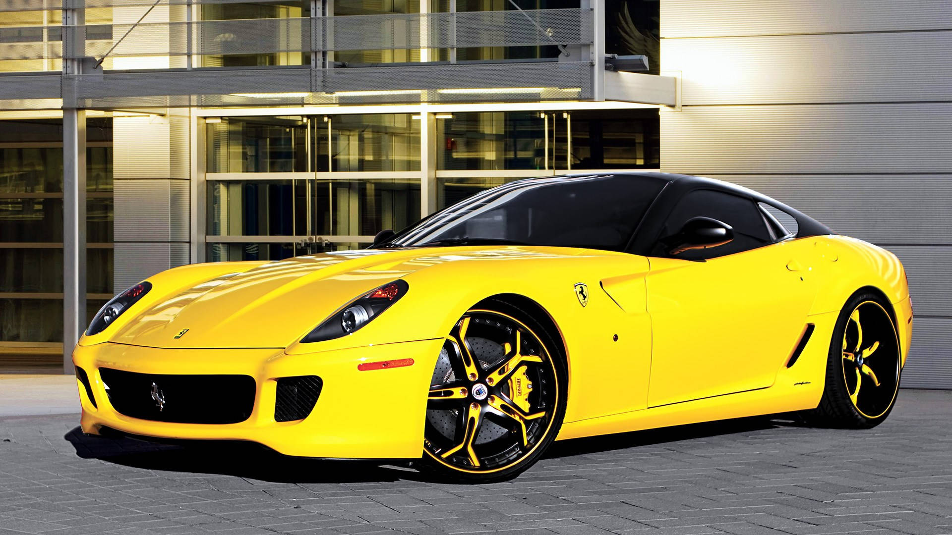 1920x1080 Ferrari 桌布 壁紙 — 一輛充滿活力的黃色法拉利跑車在現代玻璃建築旁的金色光線下閃閃發光。