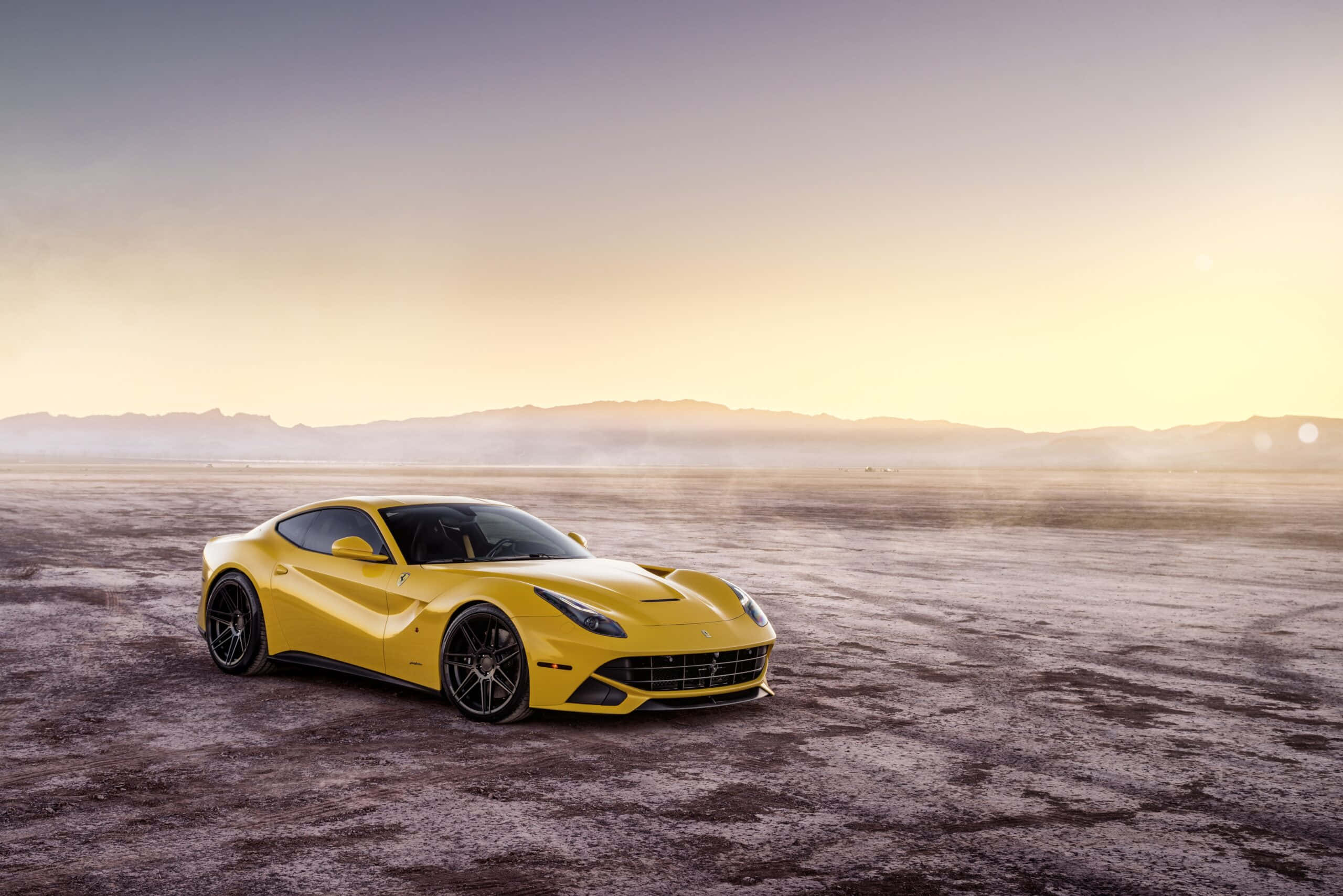 Ferrari F12 Berlinetta 桌布 壁紙 — 一輛充滿活力的黃色法拉利跑車在金色夕陽下閃耀，背景是廣闊的塵土平原和遠山。