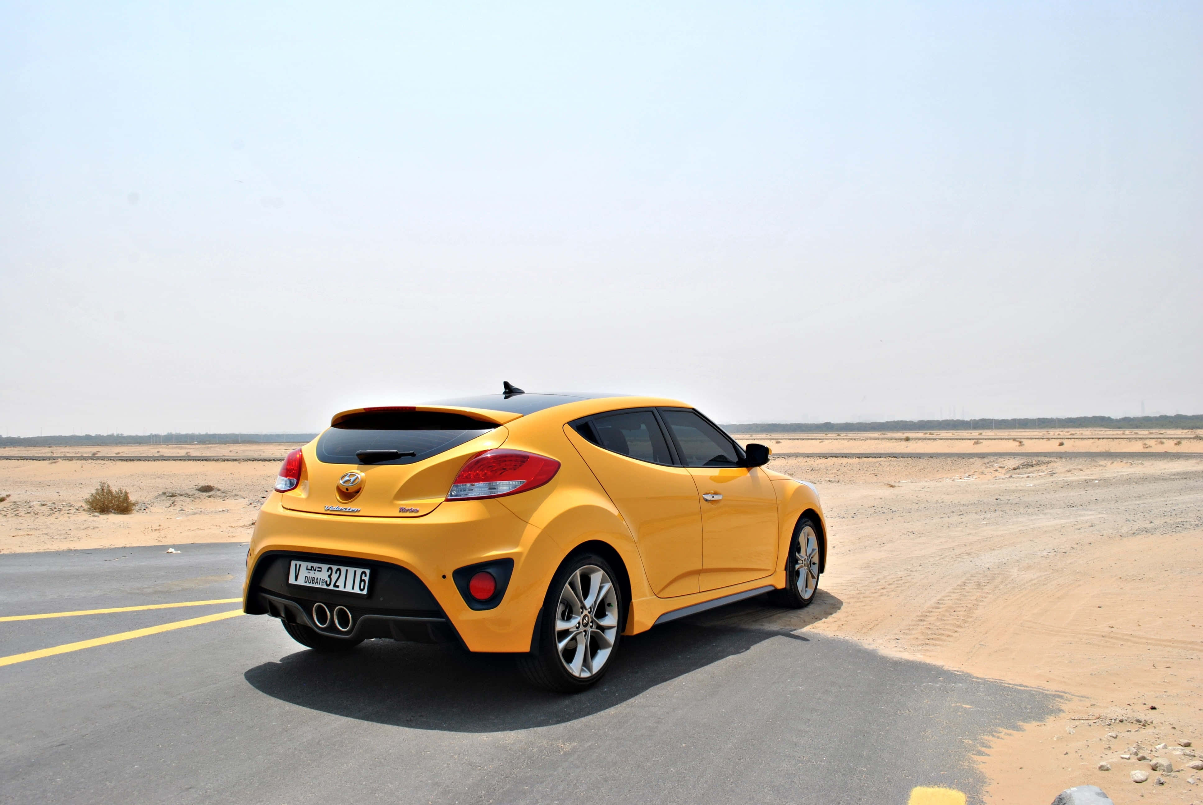Hyundai Veloster 桌布 壁紙 — 一輛充滿活力的黃色現代Veloster跑車停放在沙漠公路上，天空朦朧。