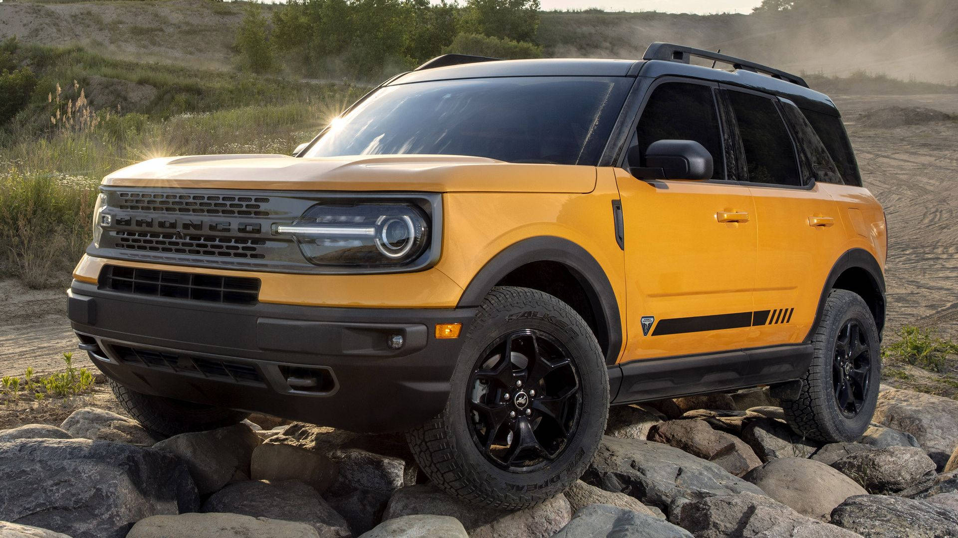 Ford Bronco 桌布 壁紙 — 一輛充滿活力的黃色福特Bronco SUV，帶有黑色飾邊和堅固輪胎，在金色陽光下征服岩石地形。