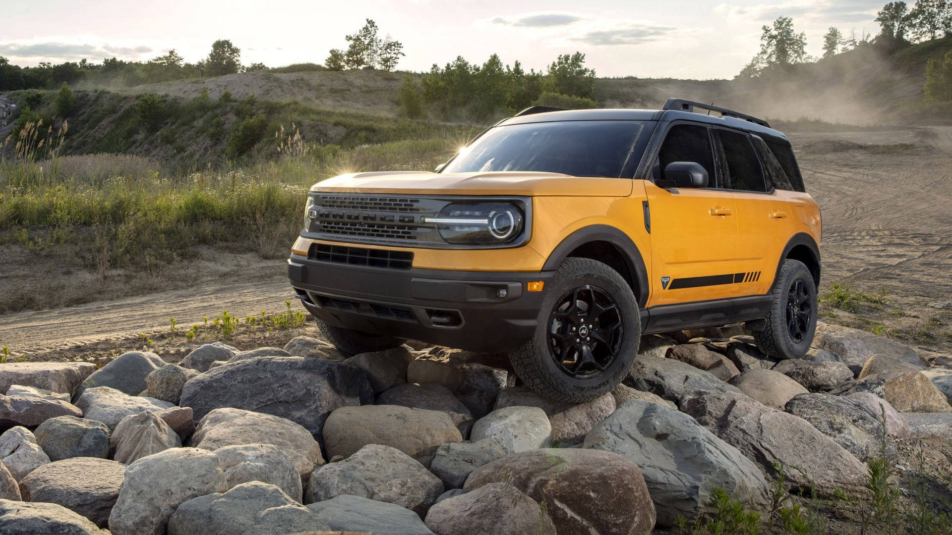Ford Bronco 桌布 壁紙 — 一輛充滿活力的黃色福特Bronco SUV征服了岩石小徑，塵土在身後飛揚，金色陽光灑滿崎嶇的地形。