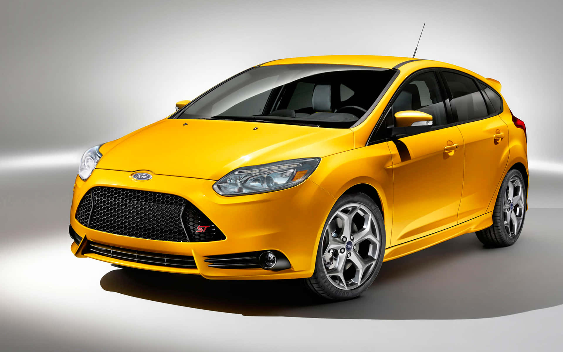 Ford Focus 桌布 壁紙 — 一輛充滿活力的黃色福特福克斯ST掀背車在極簡灰色背景的攝影棚燈光下閃閃發光。