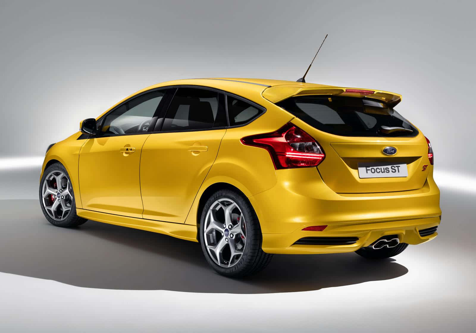 Ford Focus 桌布 壁紙 — 一輛充滿活力的黃色福特福克斯ST掀背車，在工作室燈光下展示，配有紅色尾燈和運動型合金輪圈。
