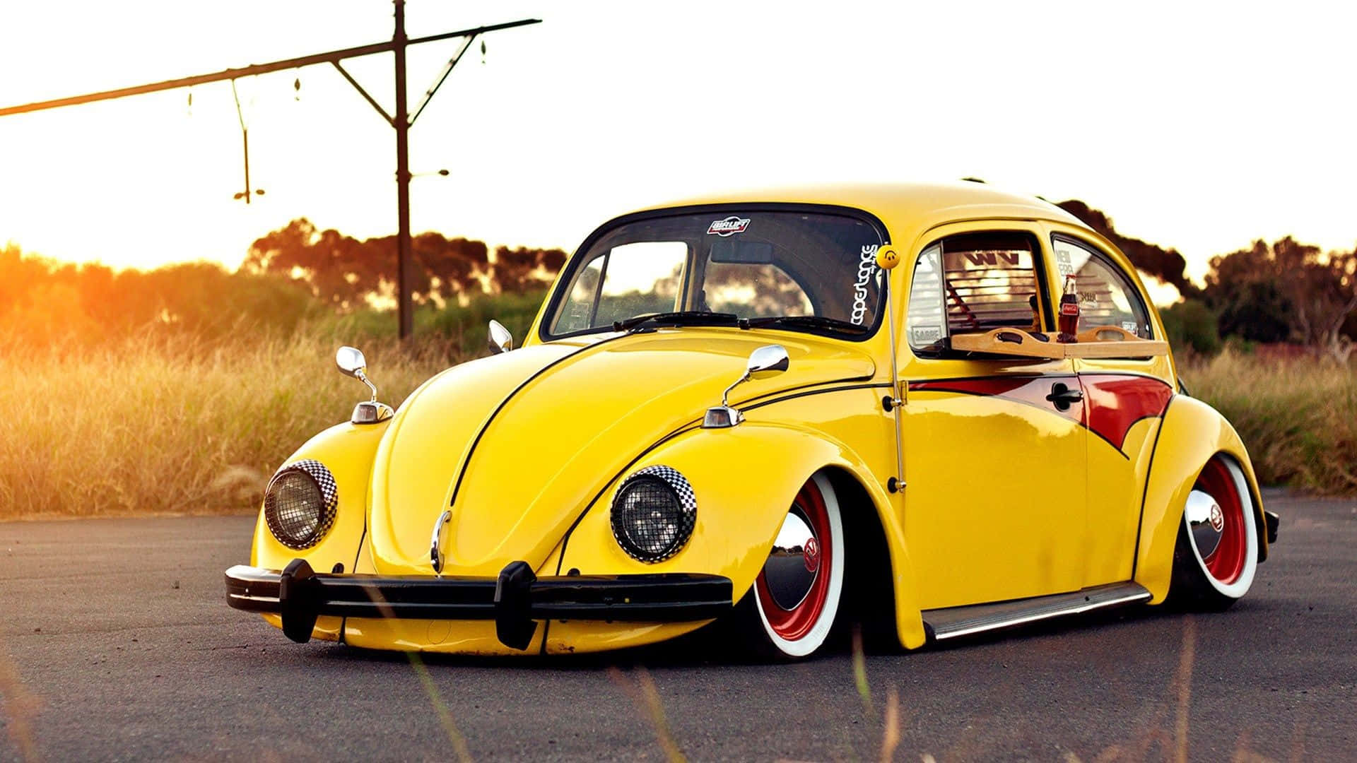 Yellow Car 桌布 壁紙 — 一輛充滿活力的黃色經典福斯金龜車，帶有紅色點綴，低矮地停在金色日落時分的道路上。
