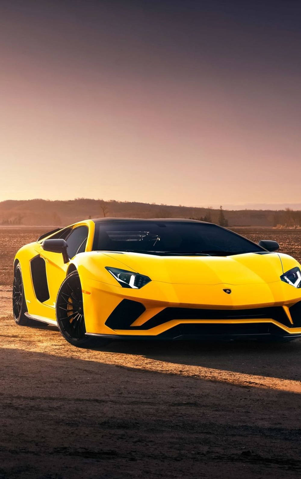 跑車 桌布 壁紙 — 一輛充滿活力的黃色藍寶堅尼Aventador在日落時分停在塵土飛揚的道路上，溫暖的金色光芒投下長長的影子。