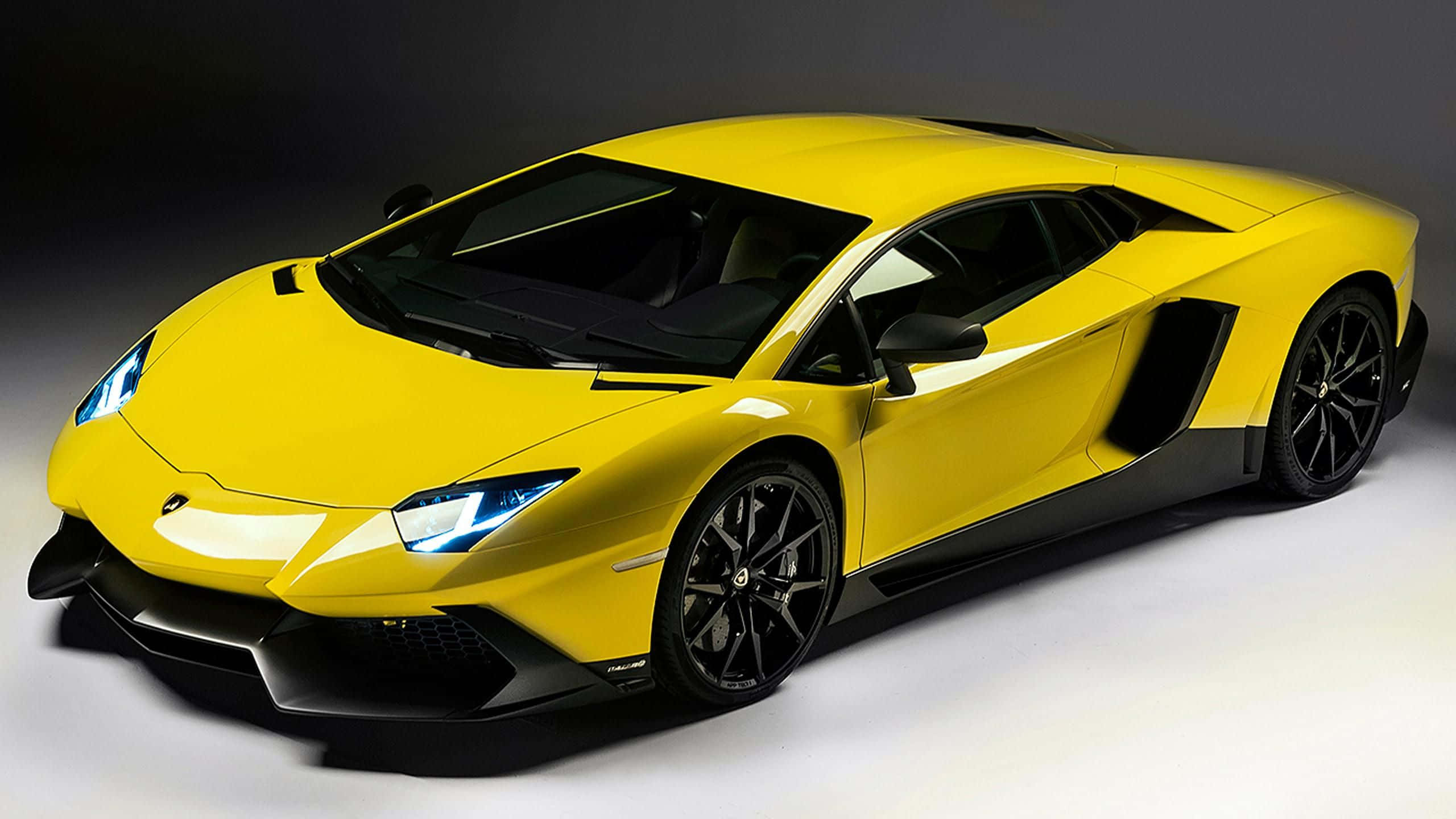 跑車 桌布 壁紙 — 一輛充滿活力的黃色藍寶堅尼Aventador跑車，帶有黑色飾邊和發光車頭燈，在深色工作室背景前擺拍。