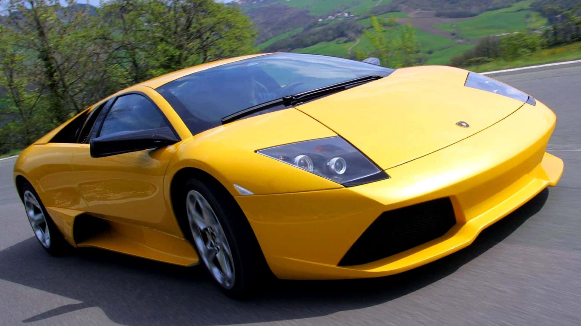 Lamborghini Murciélago 桌布 壁紙 — 一輛充滿活力的黃色藍寶堅尼Gallardo在蜿蜒的山路上疾馳，背景是鬱鬱蔥蔥的綠色山丘。