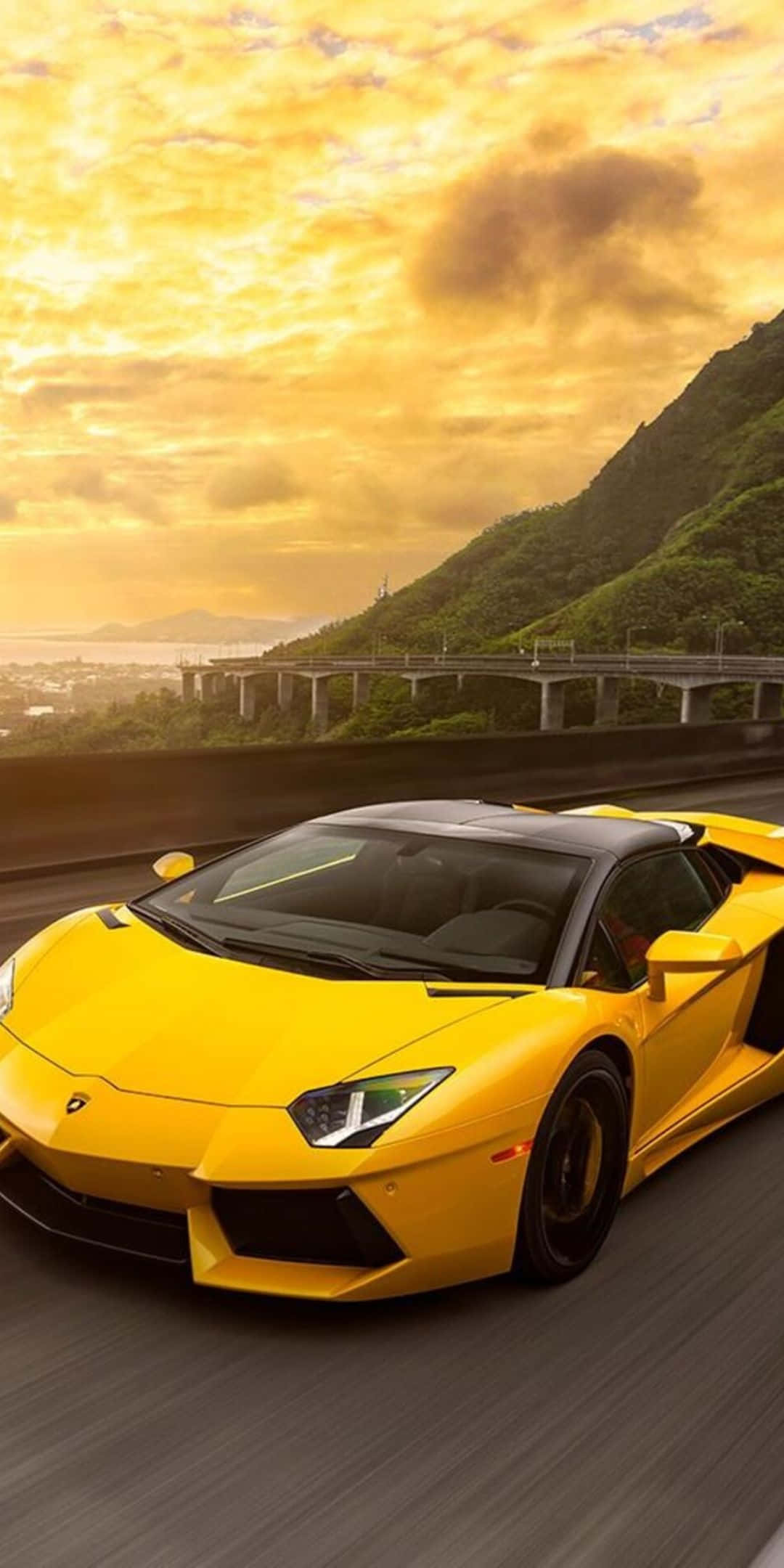Pixel 3 Lamborghini 桌布 壁紙 — 一輛充滿活力的黃色藍寶堅尼在金色日落天空下的沿海高速公路上飛馳。