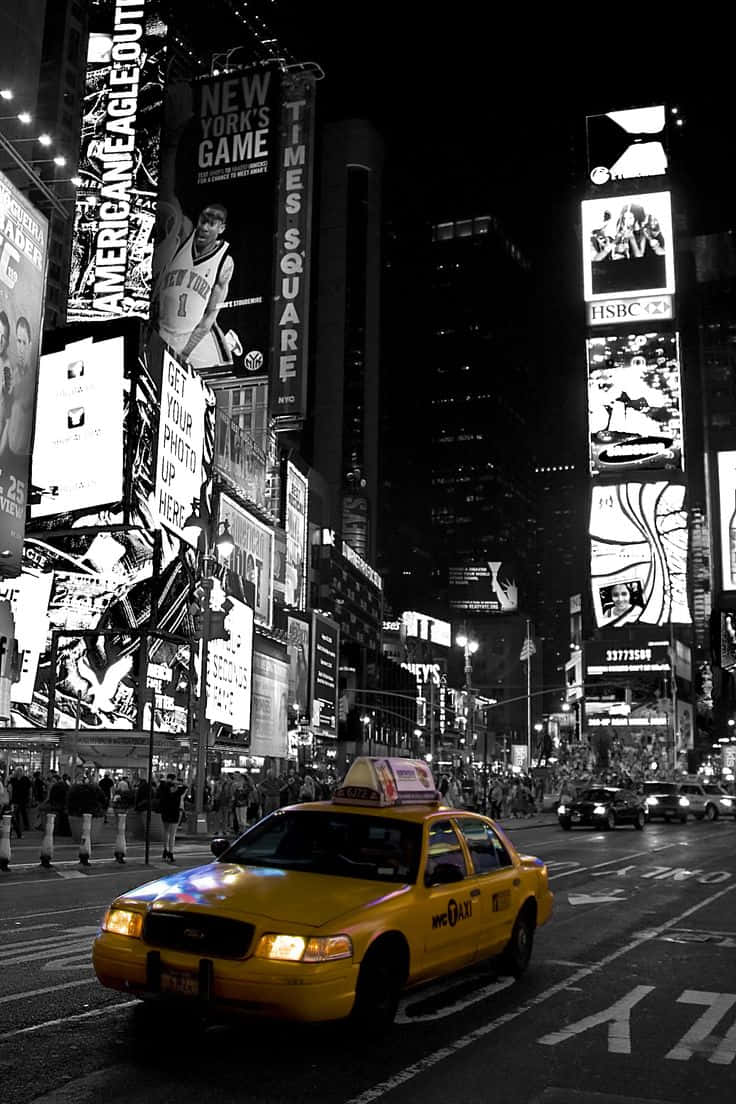 Yellow Cab 桌布 壁紙 — 一輛充滿活力的黃色計程車在夜晚穿梭於紐約市繁忙的街道，周圍環繞著高聳的燈光廣告牌和人群。