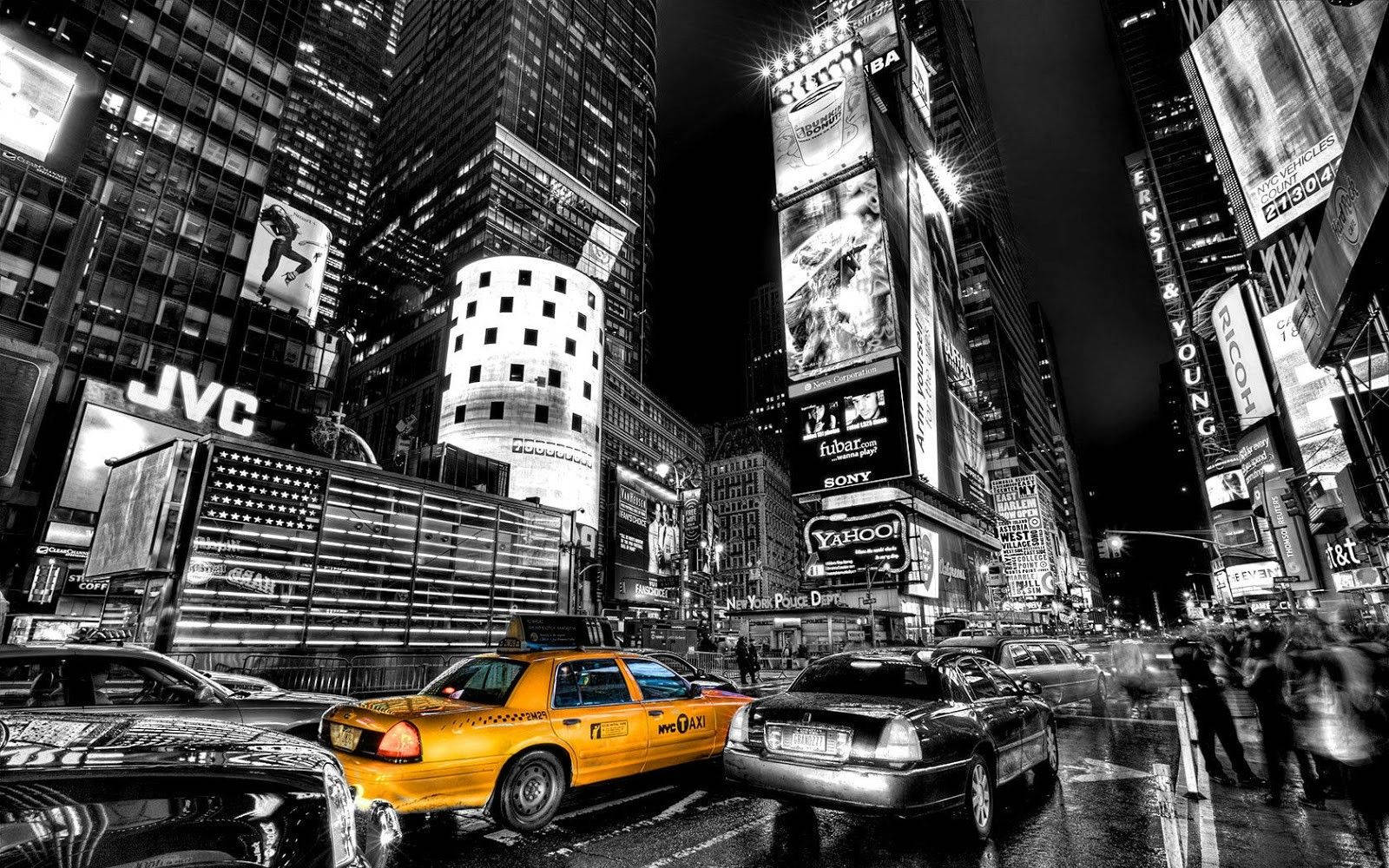 New York 桌布 壁紙 — 一輛充滿活力的黃色計程車在夜晚黑白相間、熙熙攘攘的時代廣場中脫穎而出，周圍有發光的廣告牌和濕漉漉的街道反射著城市燈光。