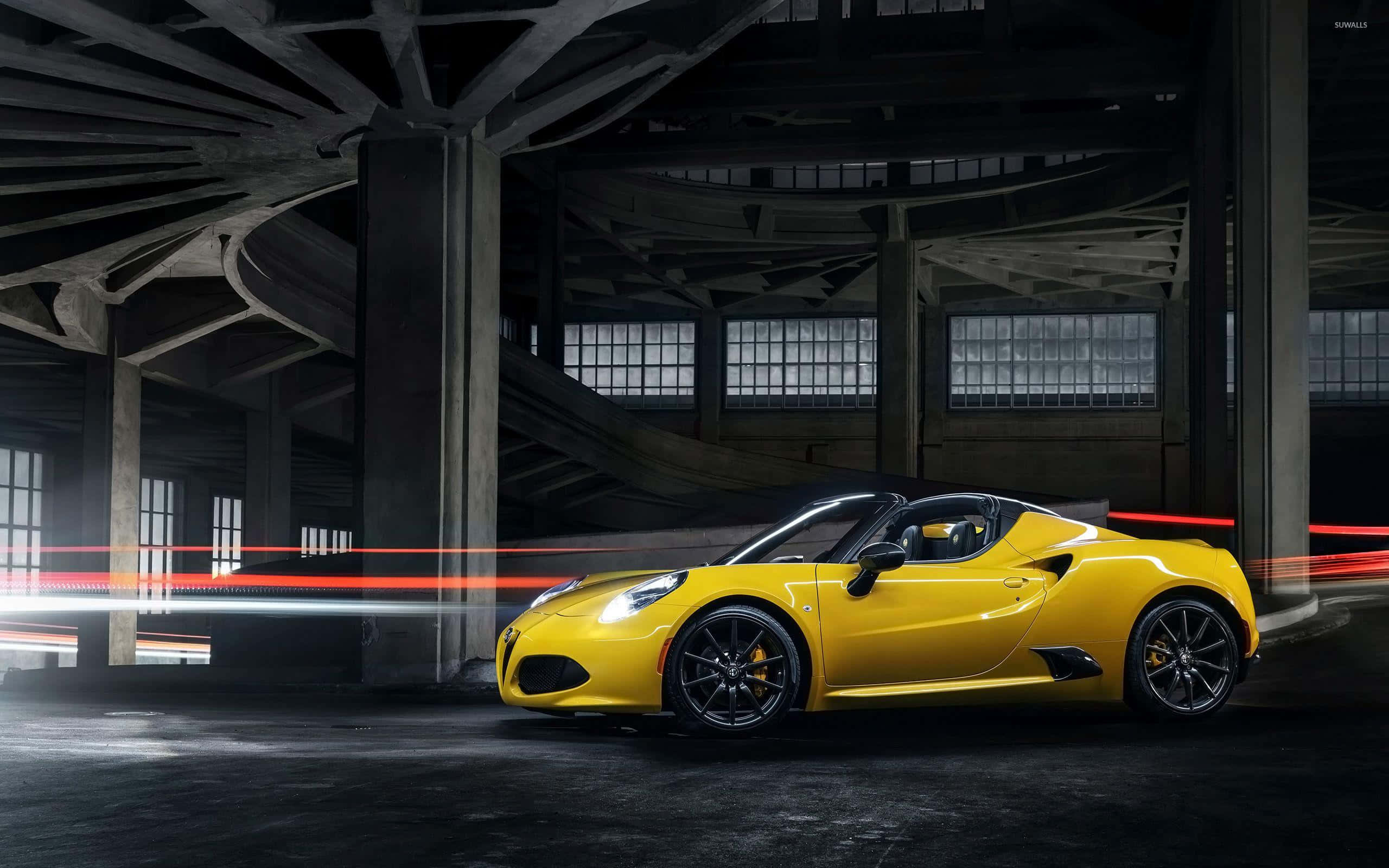 Alfa Romeo 4c 桌布 壁紙 — 一輛充滿活力的黃色跑車在昏暗的工業倉庫中穿梭，留下紅色和白色的光跡。