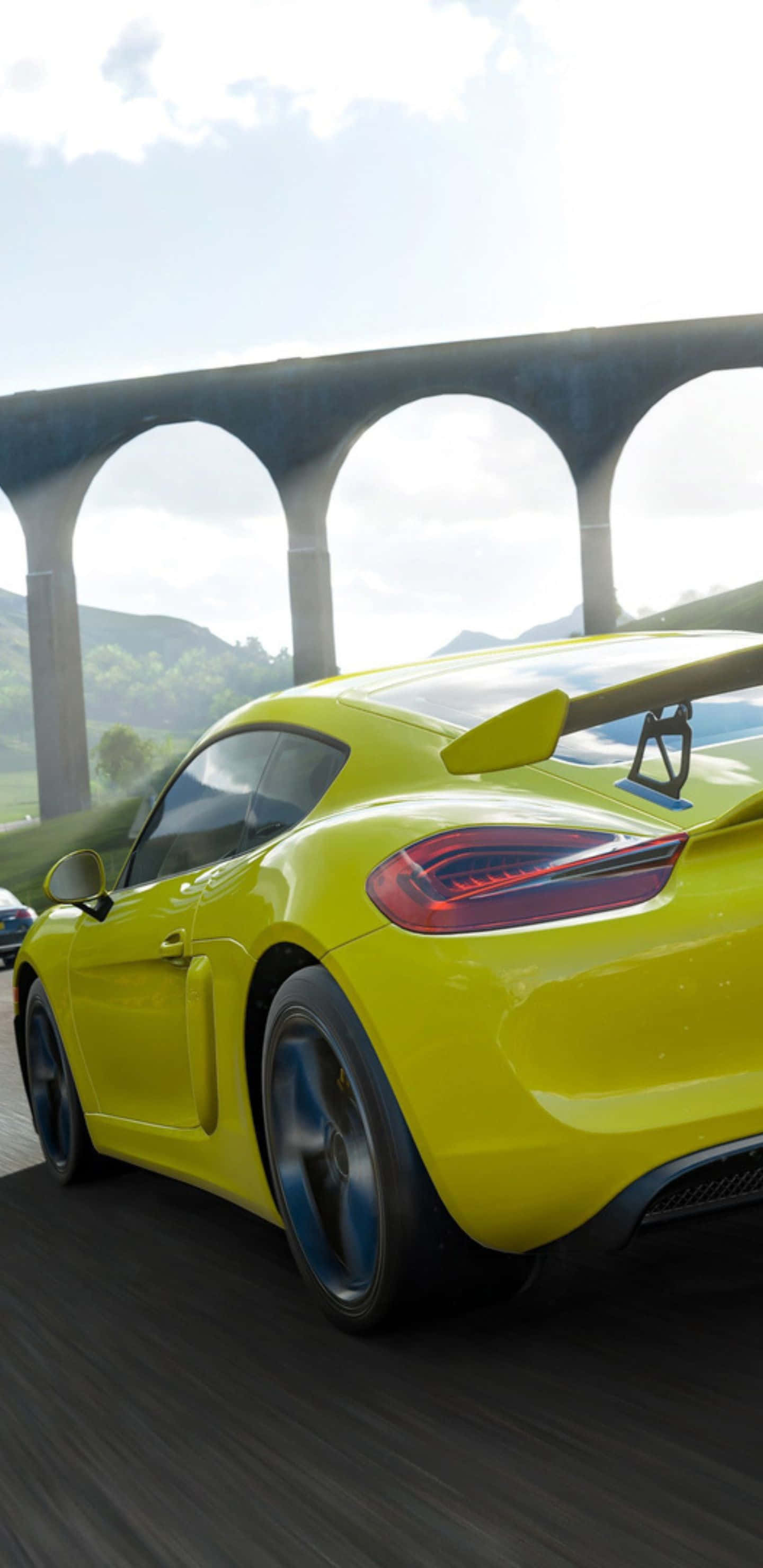 Pixel 3xl Forza Horizon 4 桌布 壁紙 — 一輛充滿活力的黃色跑車在石拱橋下疾馳，運動模糊，背景是朦朧的天空。