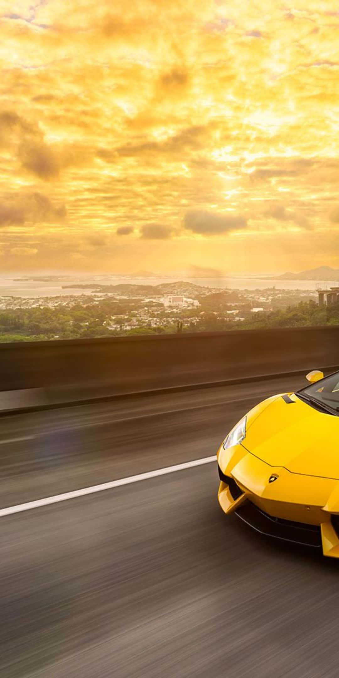 Pixel 3 Lamborghini 桌布 壁紙 — 一輛充滿活力的黃色跑車在金色夕陽天空下的沿海高速公路上飛馳。
